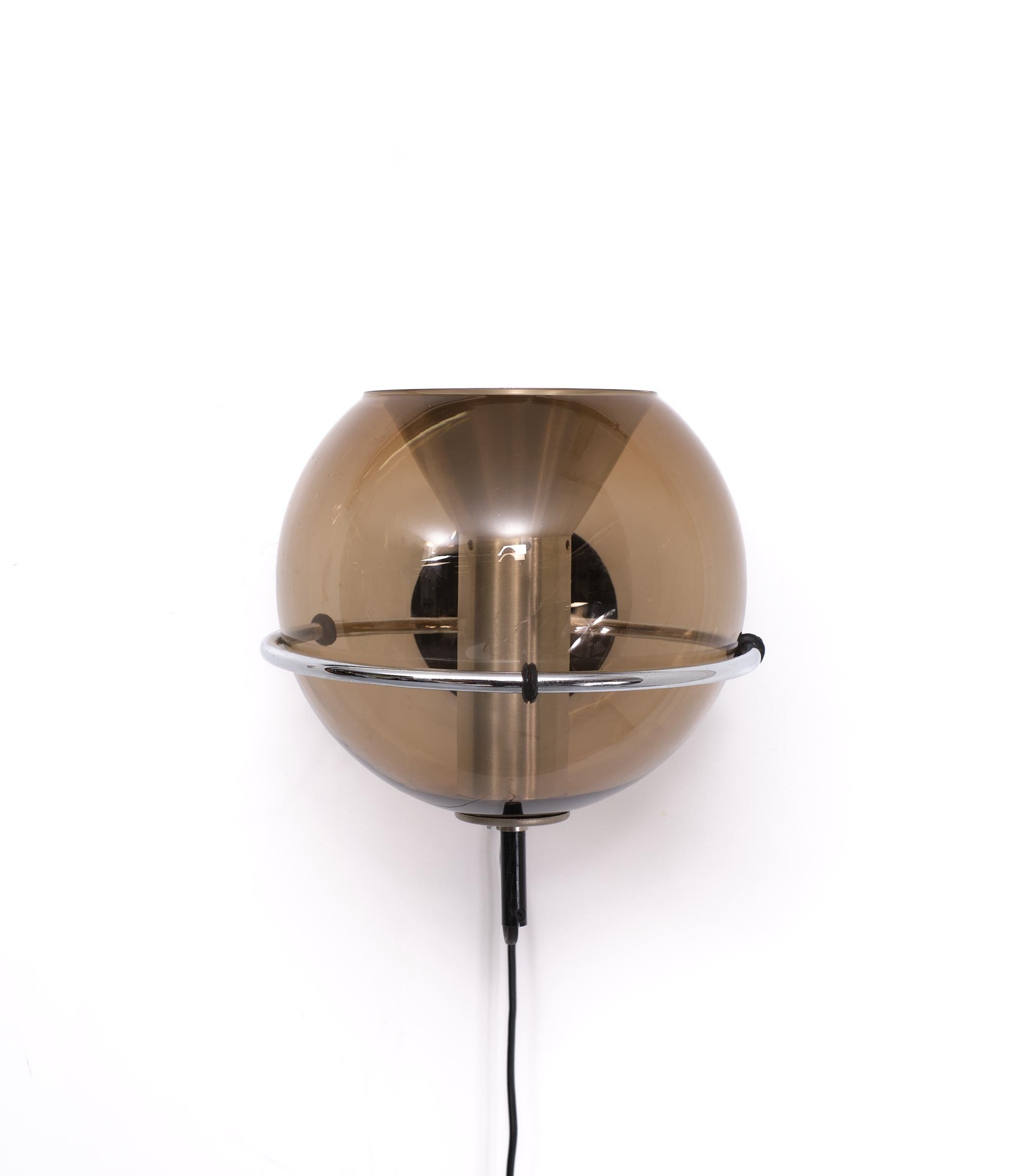 Manufactured by Raak Amsterdam Design Frank Ligtelijn . 1975  This wall lamp has a chrome wall ring that holds the smoked glass globe with aluminium diffuser shade on the inside. The wall plate is made of black painted aluminium. Lamp can shine up