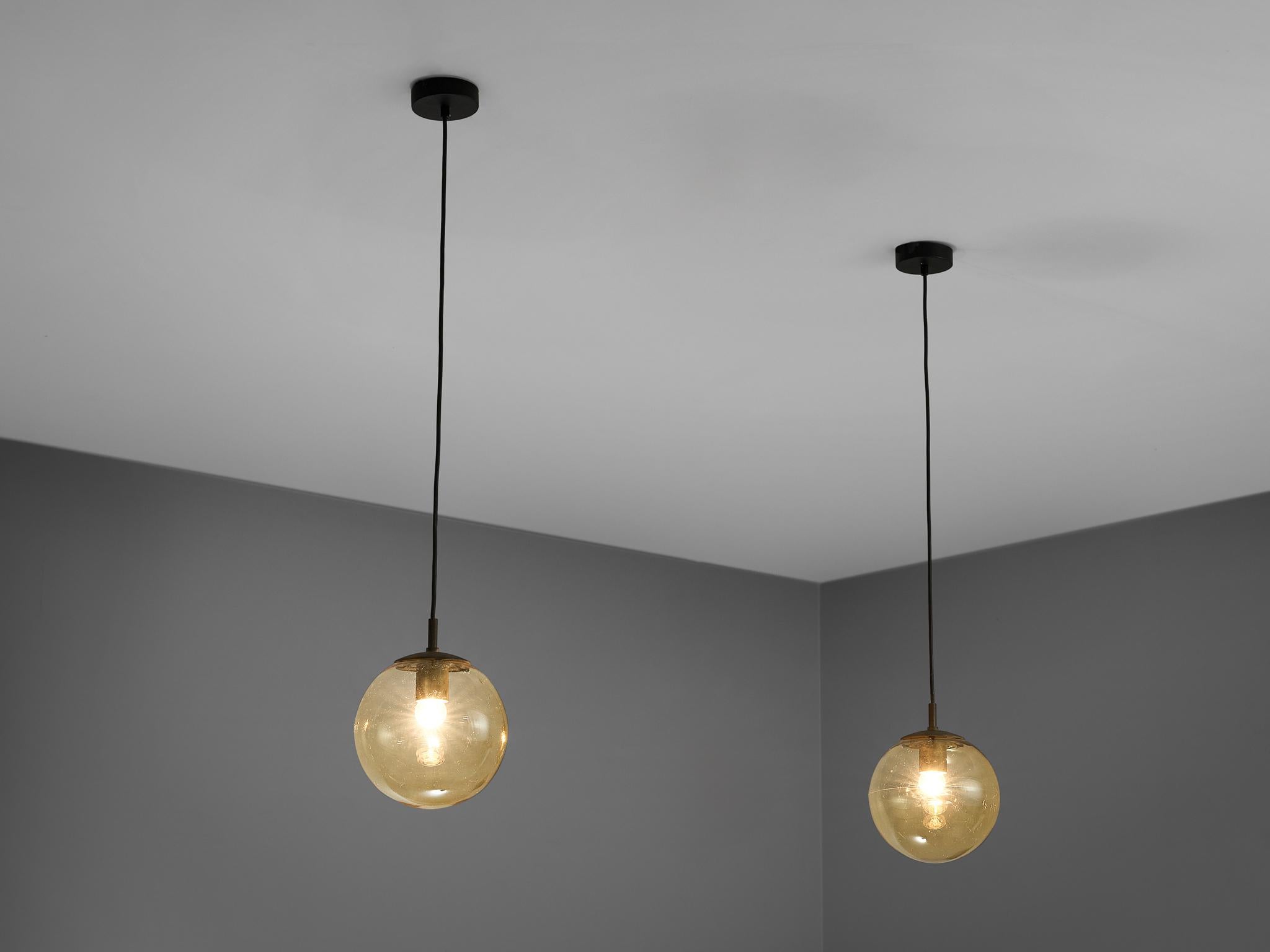 RAAK, pendant lamps, glass, brass, Europe, 1960s 

These atmospheric pendant lamps feature yellow glass. This results in a nice and soft light-tone creating a lively ambience in the room. The pendant holder is executed in brass that complements