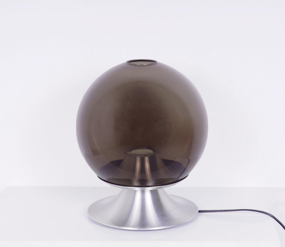 Schöne ikonische Tischlampe von Raak Amsterdam.

Modell D-2001 Dream Island, entworfen von Frank Ligtelijn in den 1960er Jahren.

Die Lampe hat einen runden Schirm aus braun-grauem Rauchglas, der auf einem Aluminiumsockel ruht.

Sehr stimmungsvolle
