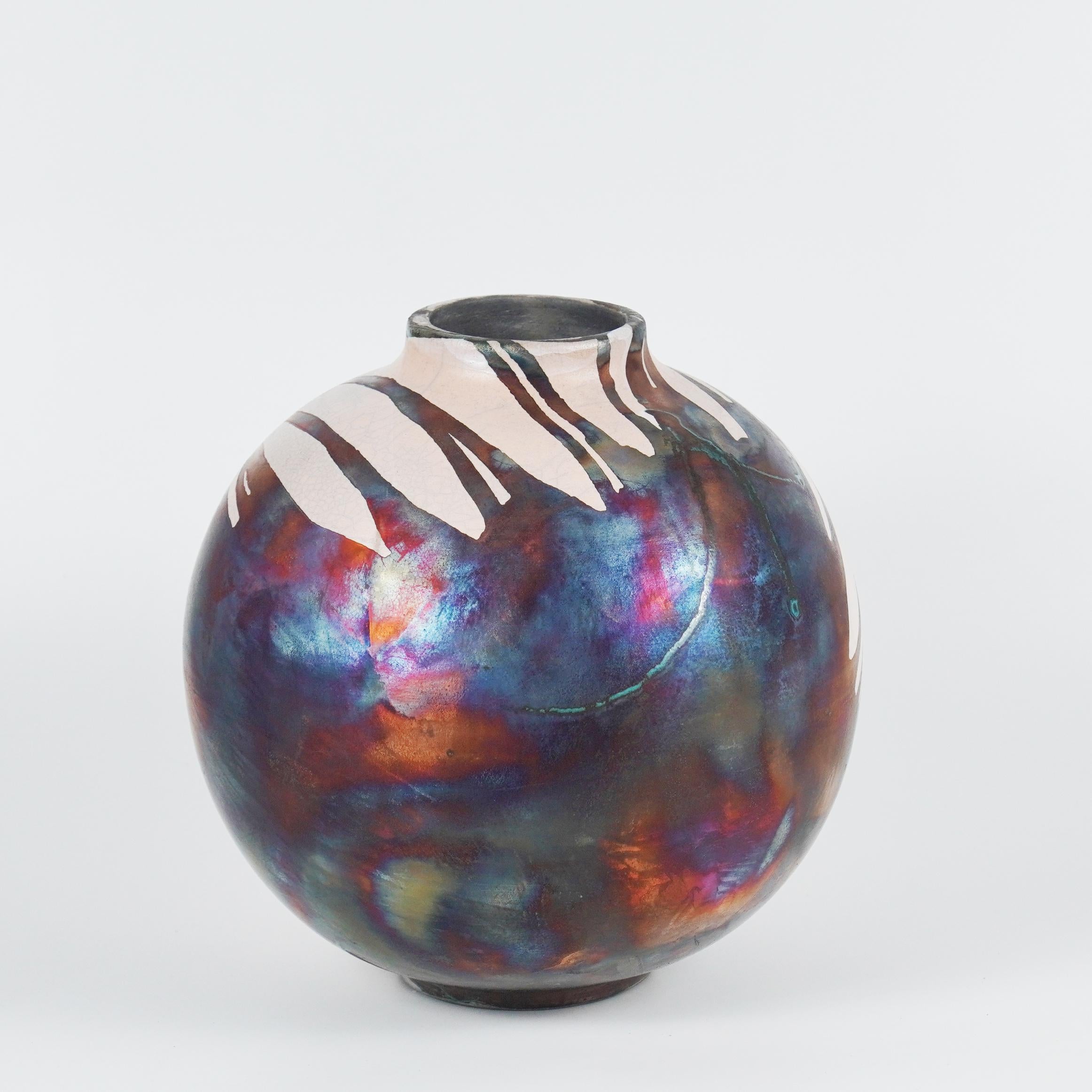 Ein faszinierender Anblick, sobald die regenbogenartigen Patinas ins Auge fallen. Diese Globe Vase ist ein rundes, geräumiges Stück, das mit der Raku-Technik hergestellt wird, was zu einer schönen, unvorhersehbaren Oberfläche führt. Diese Vase