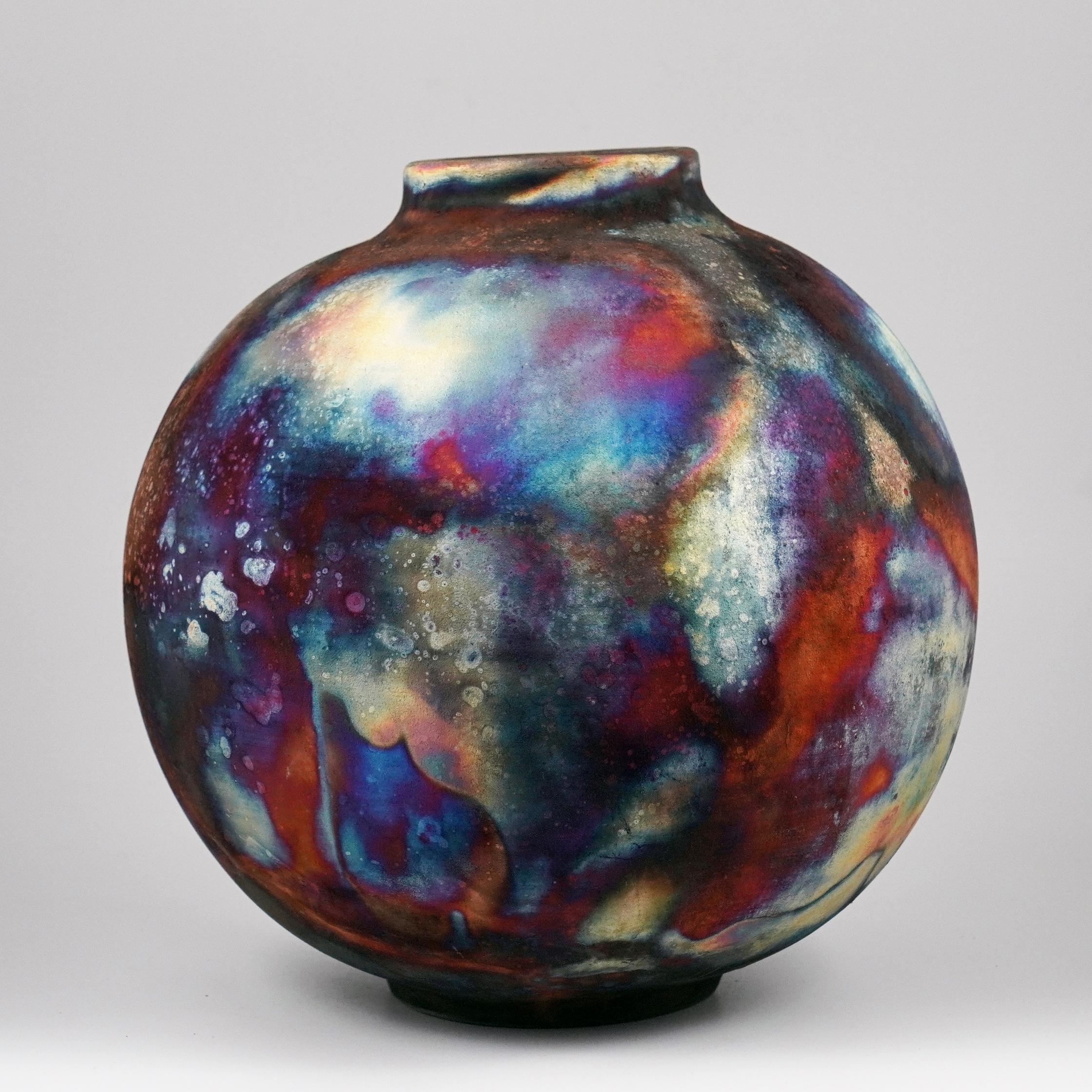 Uno spettacolo ipnotico da ammirare non appena le patine arcobaleno catturano la tua attenzione. Questo vaso Globe è un pezzo rotondo e capiente prodotto con la tecnica Raku, che dà luogo a una bellissima finitura imprevedibile. Questo vaso sarebbe