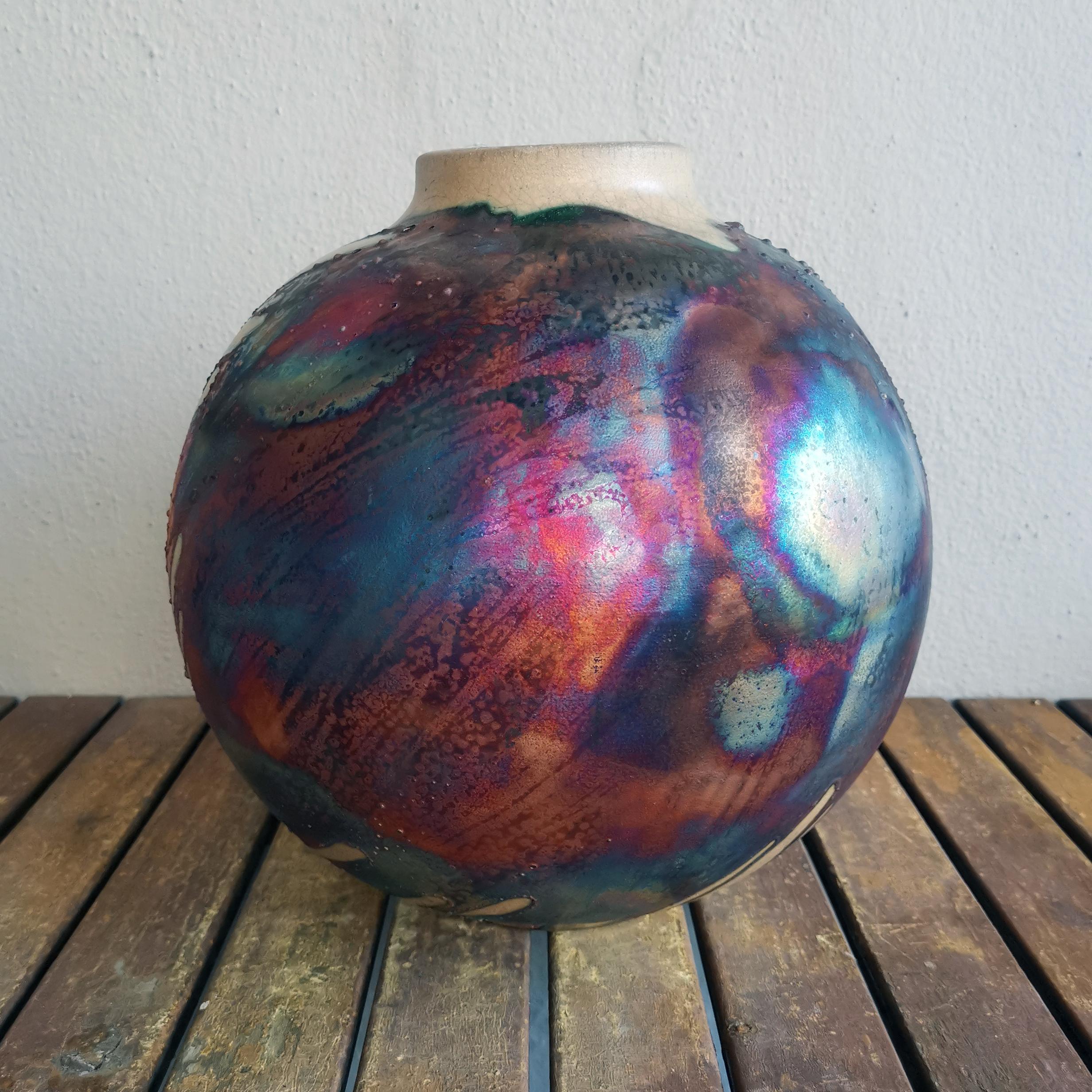 A mesmerizing sight to behold as soon as the rainbow-like patinas catch your eye. This Globe Vase is a round, capacious piece produced using the Raku technique, resulting in a beautiful unpredictable finish. This vase would be the perfect