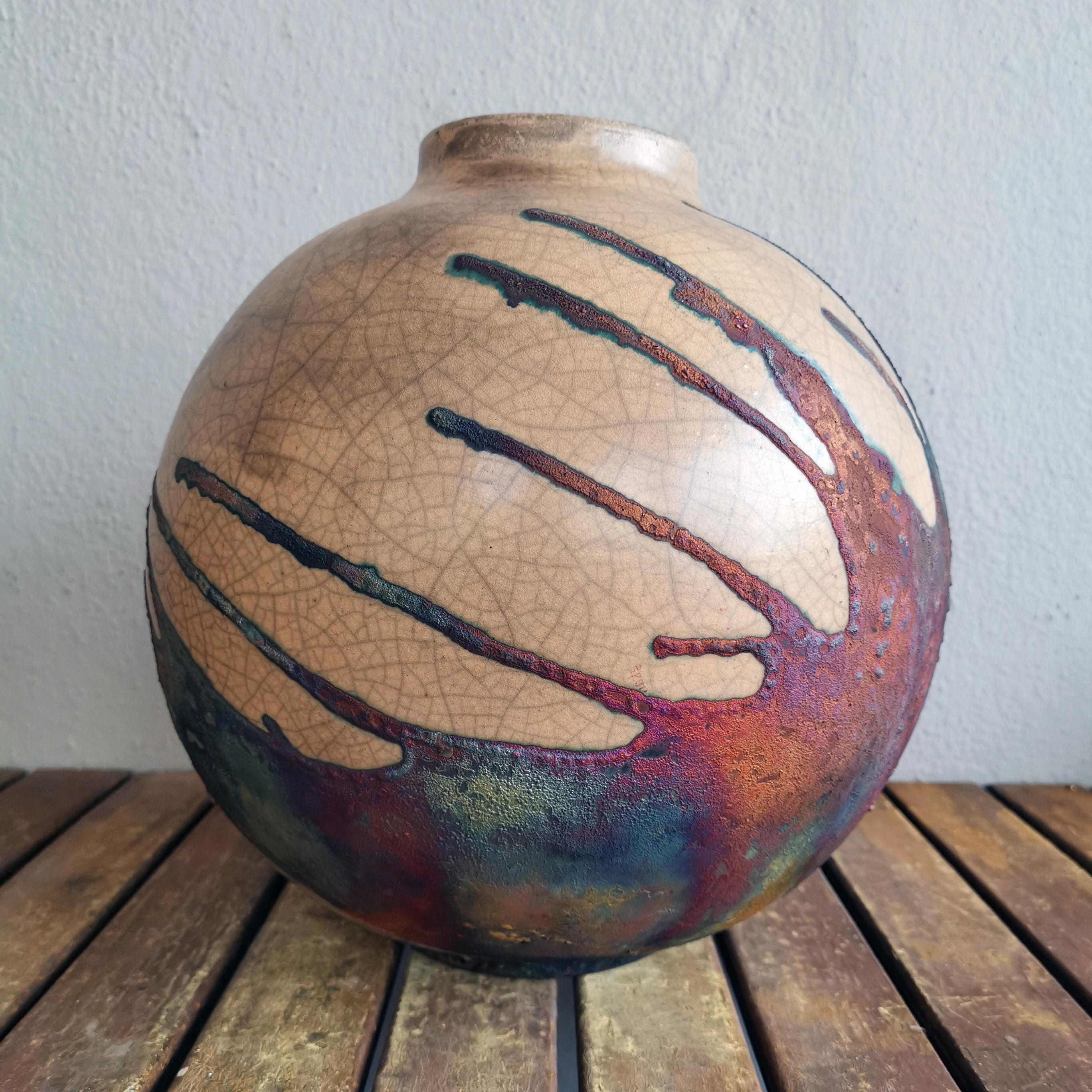 Ein faszinierender Anblick, sobald die regenbogenartigen Patinas ins Auge fallen. Diese Globe Vase ist ein rundes, geräumiges Stück, das mit der Raku-Technik hergestellt wird, was zu einer schönen, unvorhersehbaren Oberfläche führt. Diese Vase