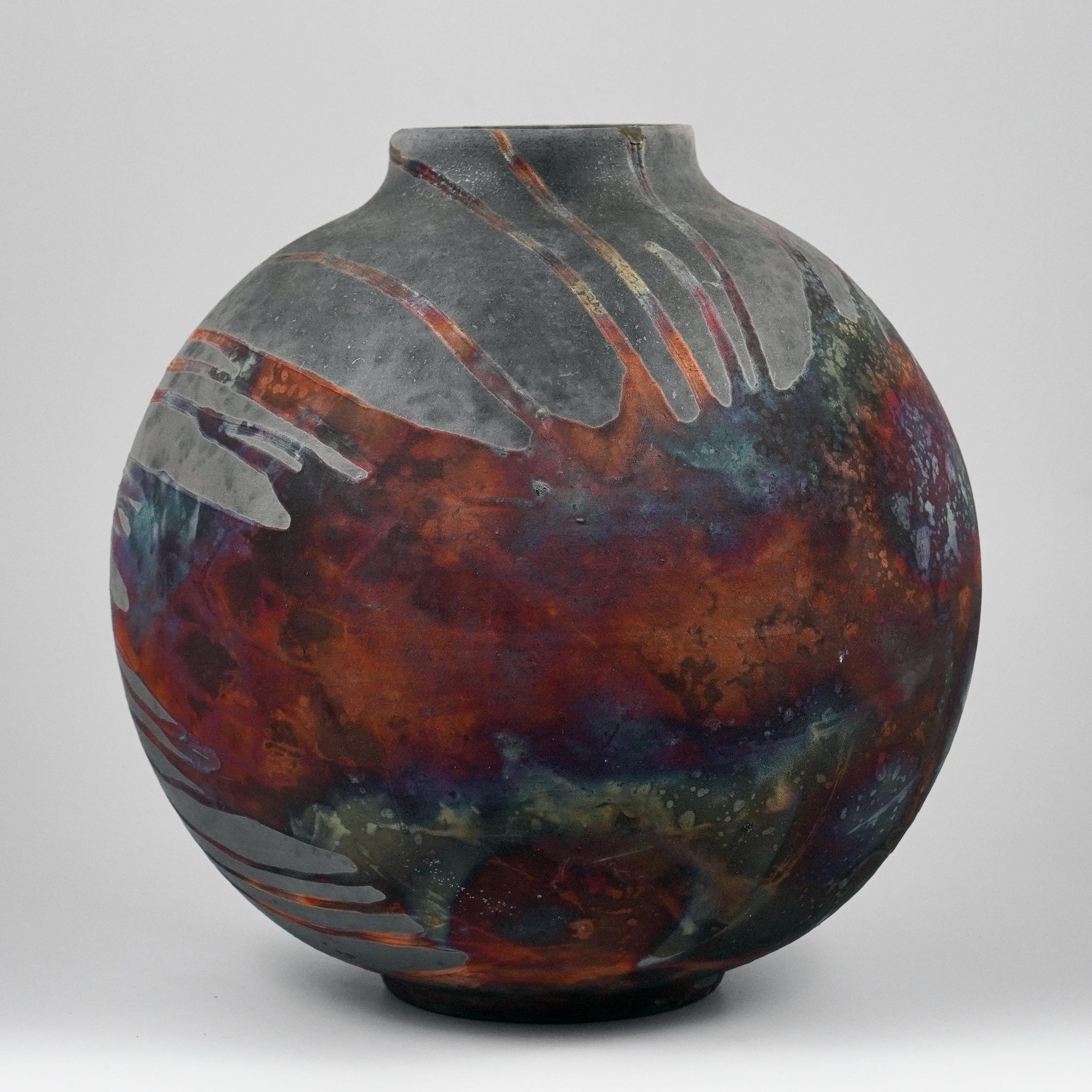 Un spectacle fascinant à contempler dès que les patines en forme d'arc-en-ciel attirent votre attention. Ce vase Globe est une pièce ronde et volumineuse produite à l'aide de la technique Raku, ce qui donne une belle finition imprévisible. Ce vase