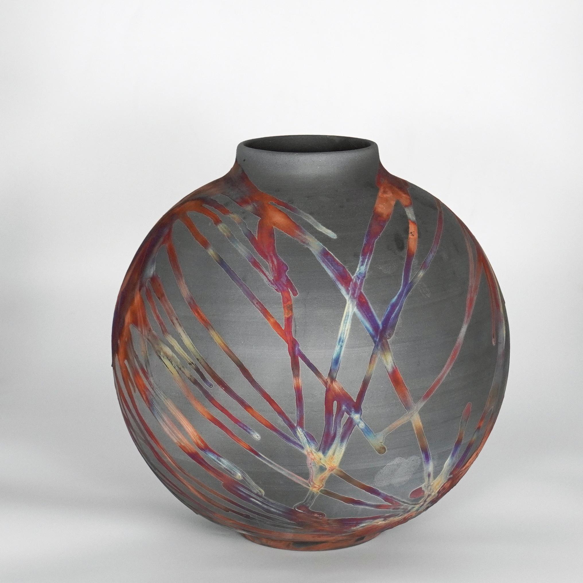 A mesmerizing sight to behold as soon as the rainbow-like patinas catch your eye. This Globe Vase is a round, capacious piece produced using the Raku technique, resulting in a beautiful unpredictable finish. This vase would be the perfect