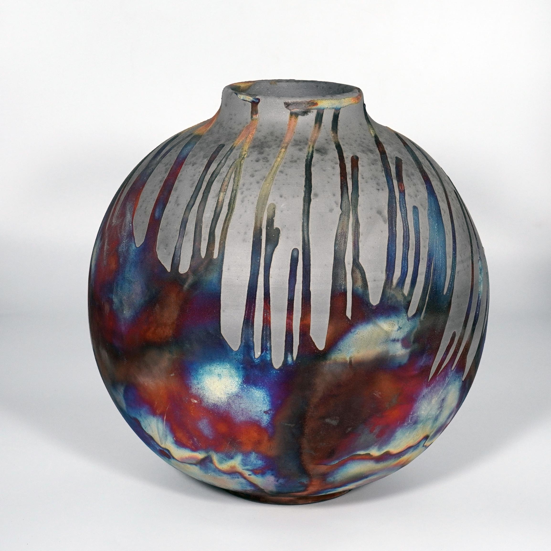A mesmerizing sight to behold as soon as the rainbow-like patinas catch your eye. This Globe Vase is a round, capacious piece produced using the Raku technique, resulting in a beautiful unpredictable finish. This vase would be the perfect