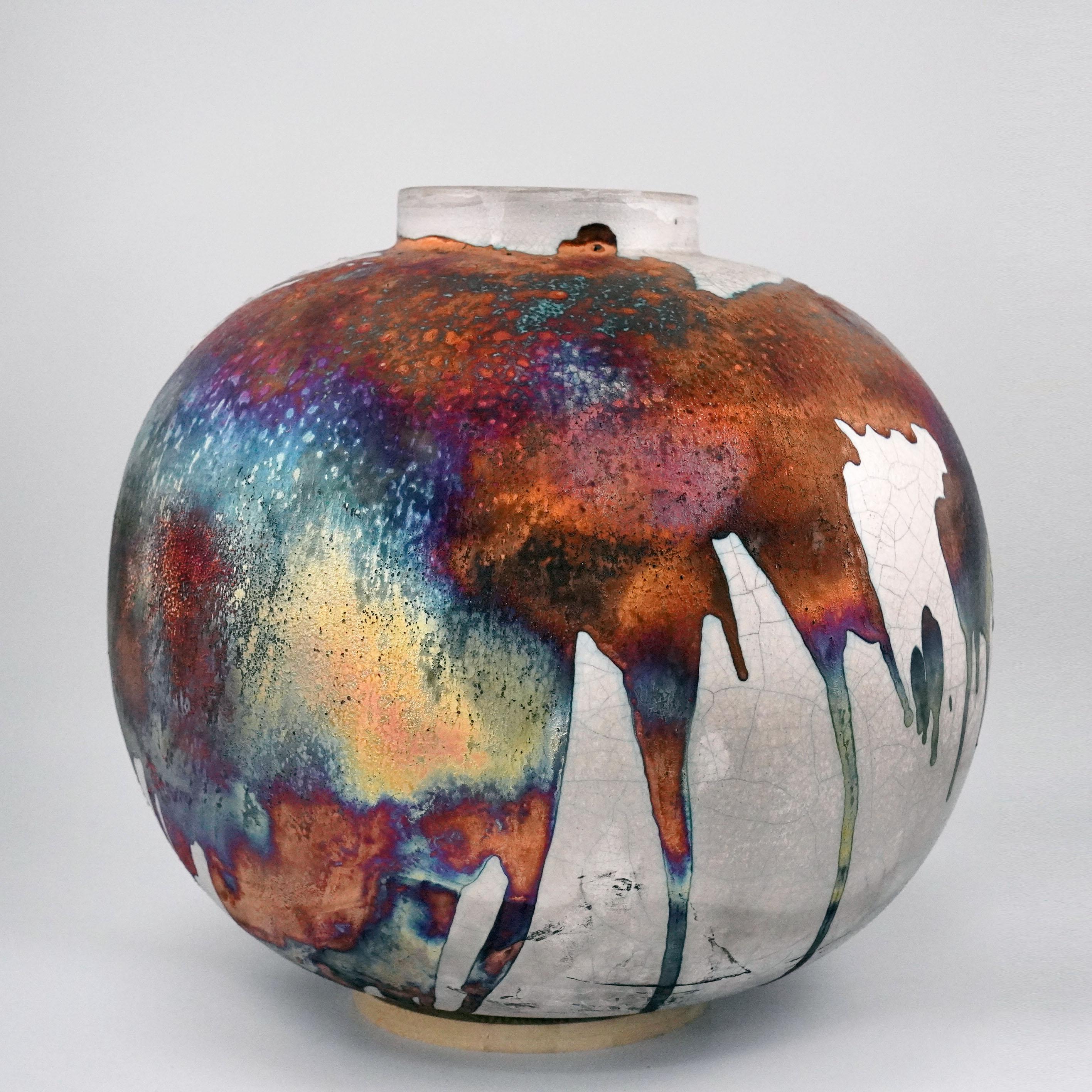 Ein faszinierender Anblick, sobald die regenbogenartigen Patinas ins Auge fallen. Die Globe XL Vase ist ein rundes, geräumiges Stück, das mit der Raku-Technik hergestellt wird, was zu einer schönen, unvorhersehbaren Oberfläche führt. Diese Vase