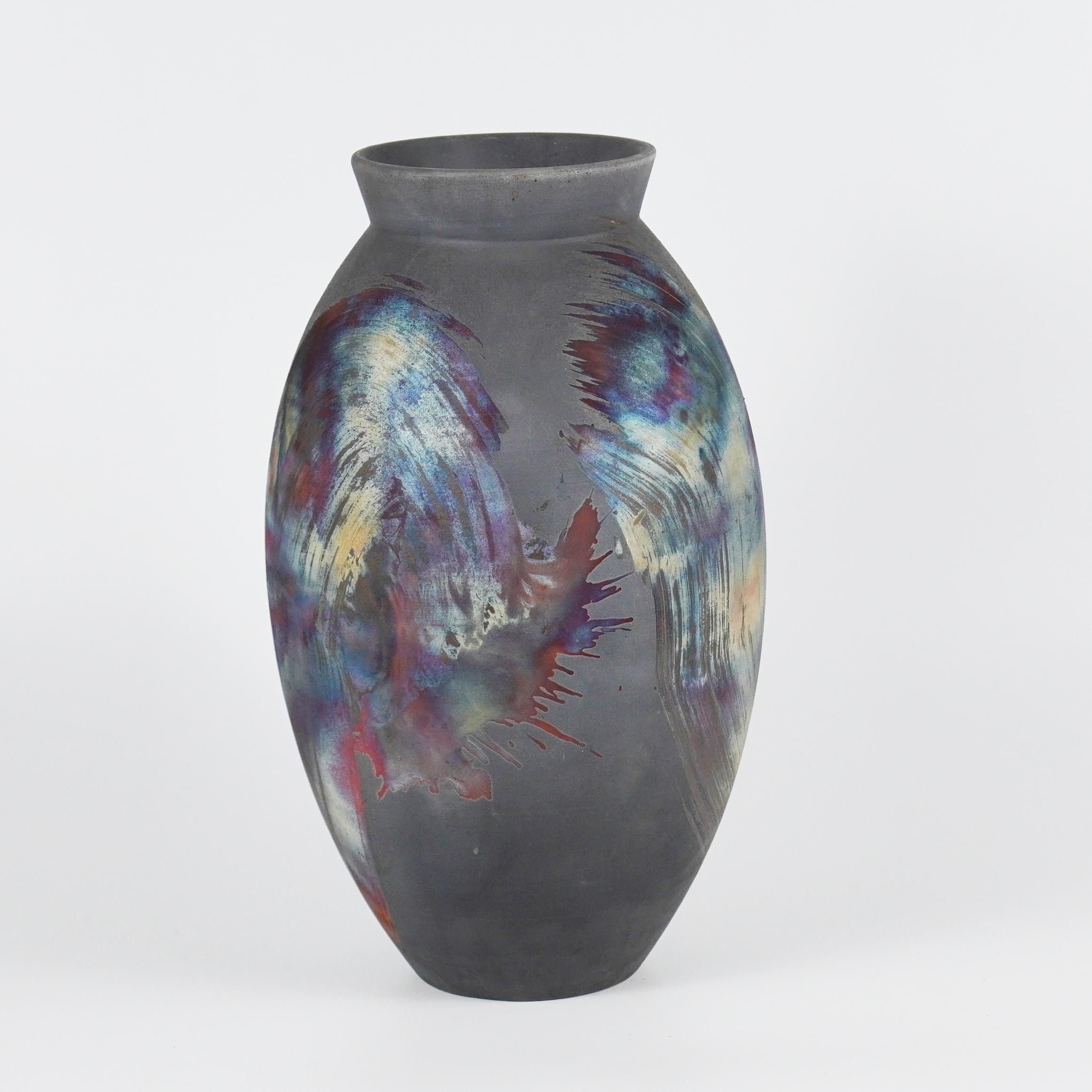 A mesmerizing sight to behold as soon as the rainbow-like patinas catch your eye. The oval vase is a tall, teardrop-shaped design best for adding a touch of elegance and intrigue to an interior space. Made using the Raku technique, it easily becomes