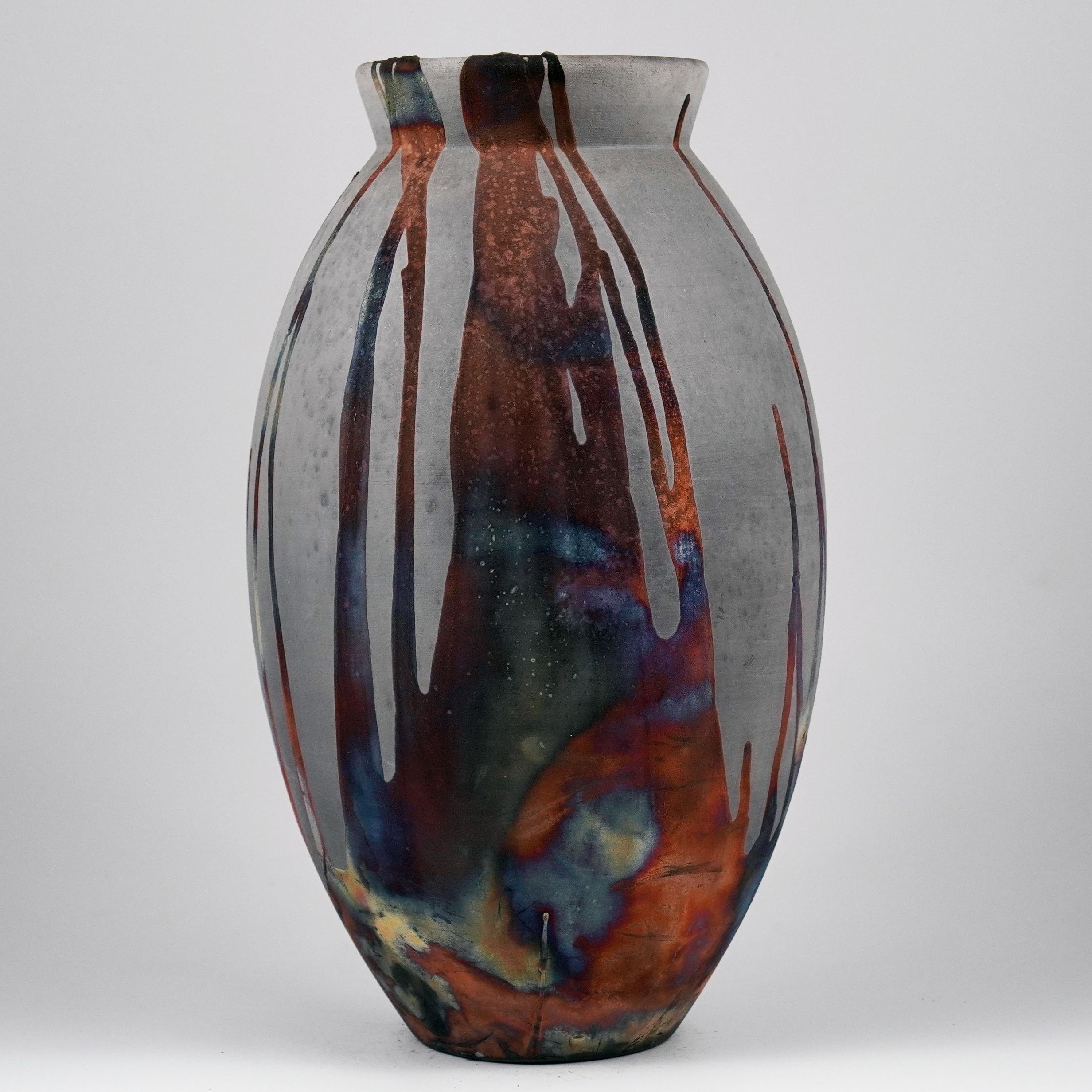A mesmerizing sight to behold as soon as the rainbow-like patinas catch your eye. The oval vase is a tall, teardrop-shaped design best for adding a touch of elegance and intrigue to an interior space. Made using the Raku technique, it easily becomes