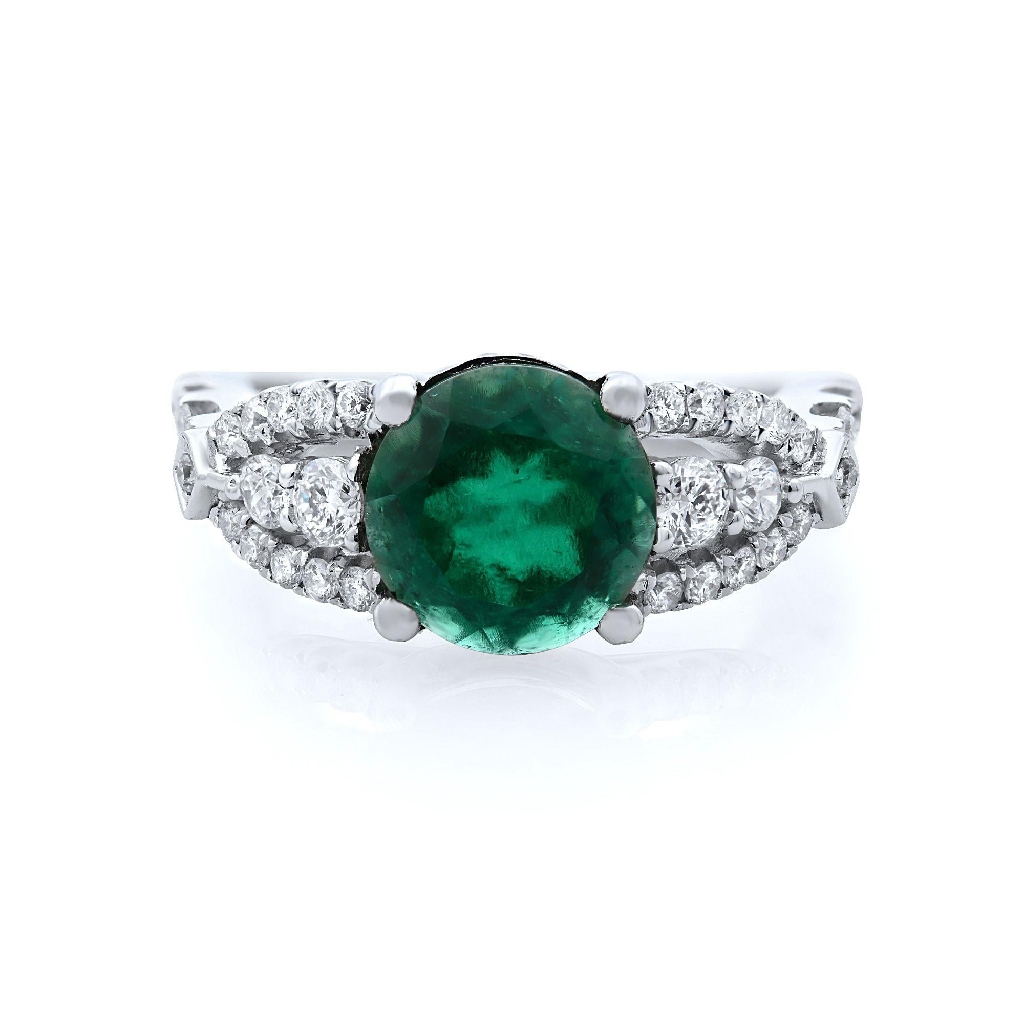 This 18K white gold engagement ring features a central round cut green emerald resting delicately with sparkling round diamonds and flanked by two rows of round accent diamonds. Diamond carat weight 1.00ct. Emerald weight 1.90ct. Ring size 6.75.
