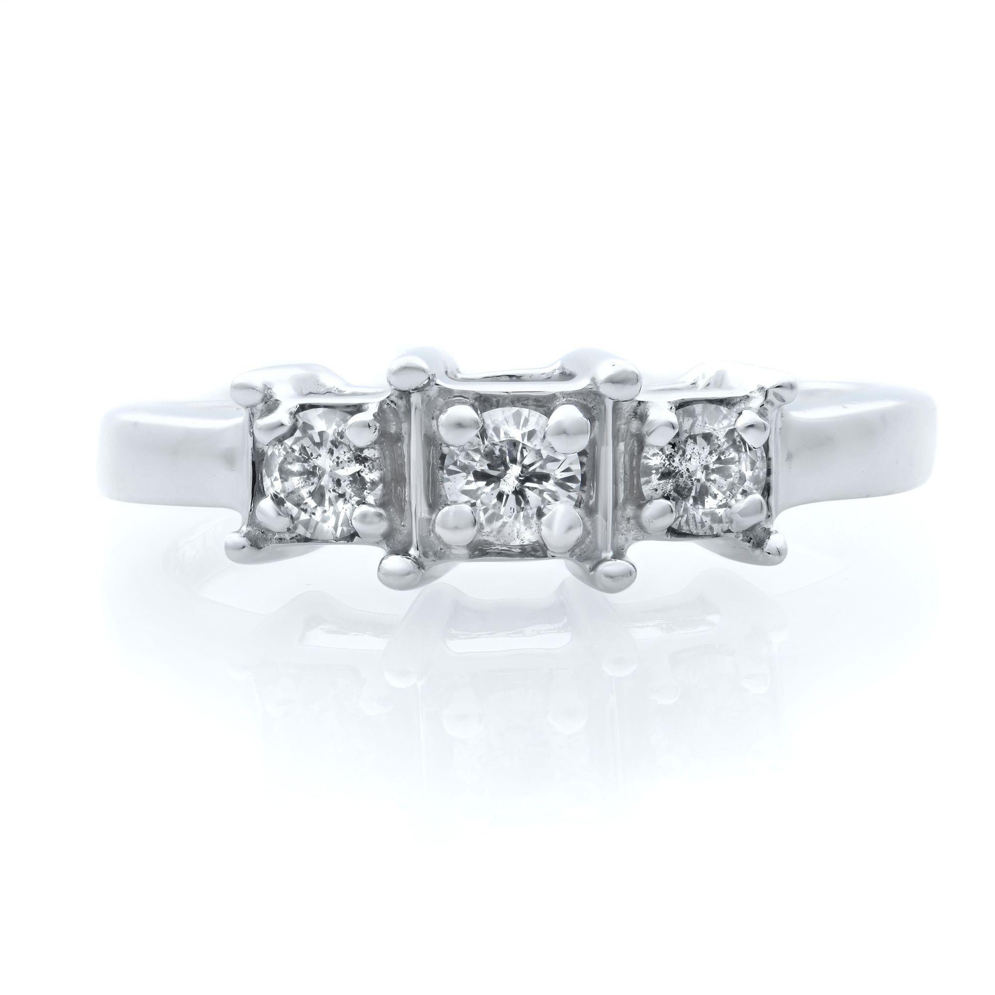 This stunning engagement ring features a round brilliant cut diamond prong set at the top, with a smaller round diamond prong set on either side to complete the three-stone setting. The setting is square looking, bu the stones are round. Total carat