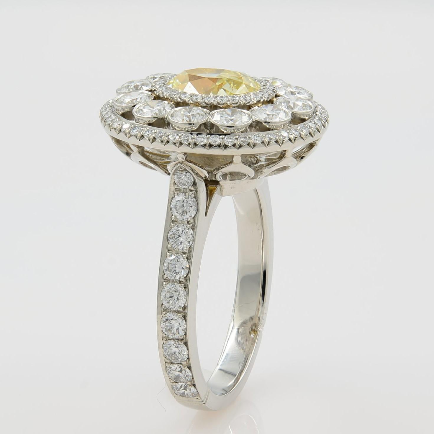 This beautiful piece features a one-carat light fancy yellow diamond surrounded by three rows of round brilliant diamonds alternating between pave set and bezel set in each row. Set in a bright-cut pave shank composition accented with more sparkling