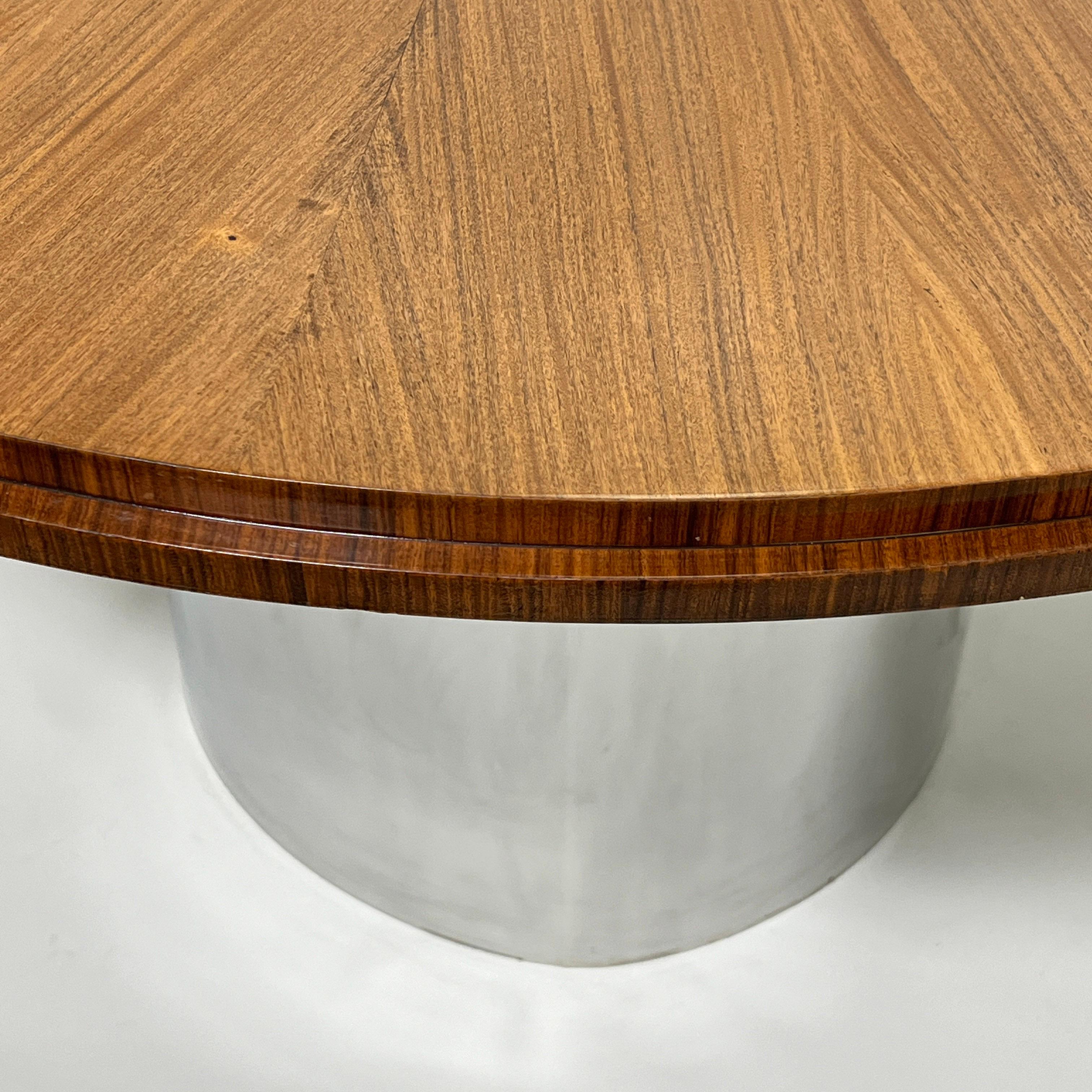 A 1970s custom made expanding dining table in the manner of Karl Springer. The top, veneered in mahogany with a wenge edge, rests upon a custom chromed steel pedestal. It is expandable from 50” without leaves to 74” with five book-matched elbow