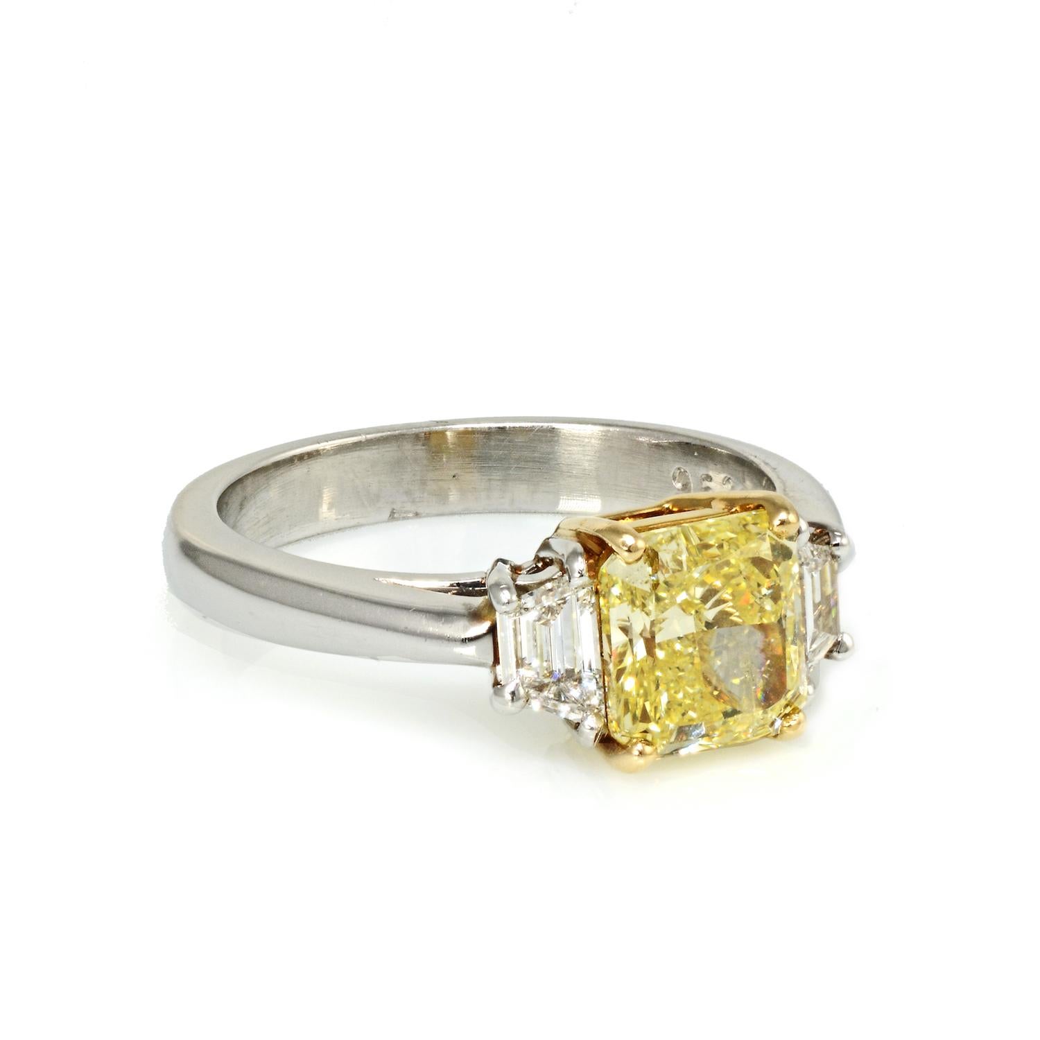Ladies beautiful platinum and yellow gold three stone diamond ring featuring a 1.60 carat Radiant-cut diamond of Fancy Intense Yellow color. The center stone is flanked by trapezoid cut diamonds weighing approximately 0.32 carats total weight of