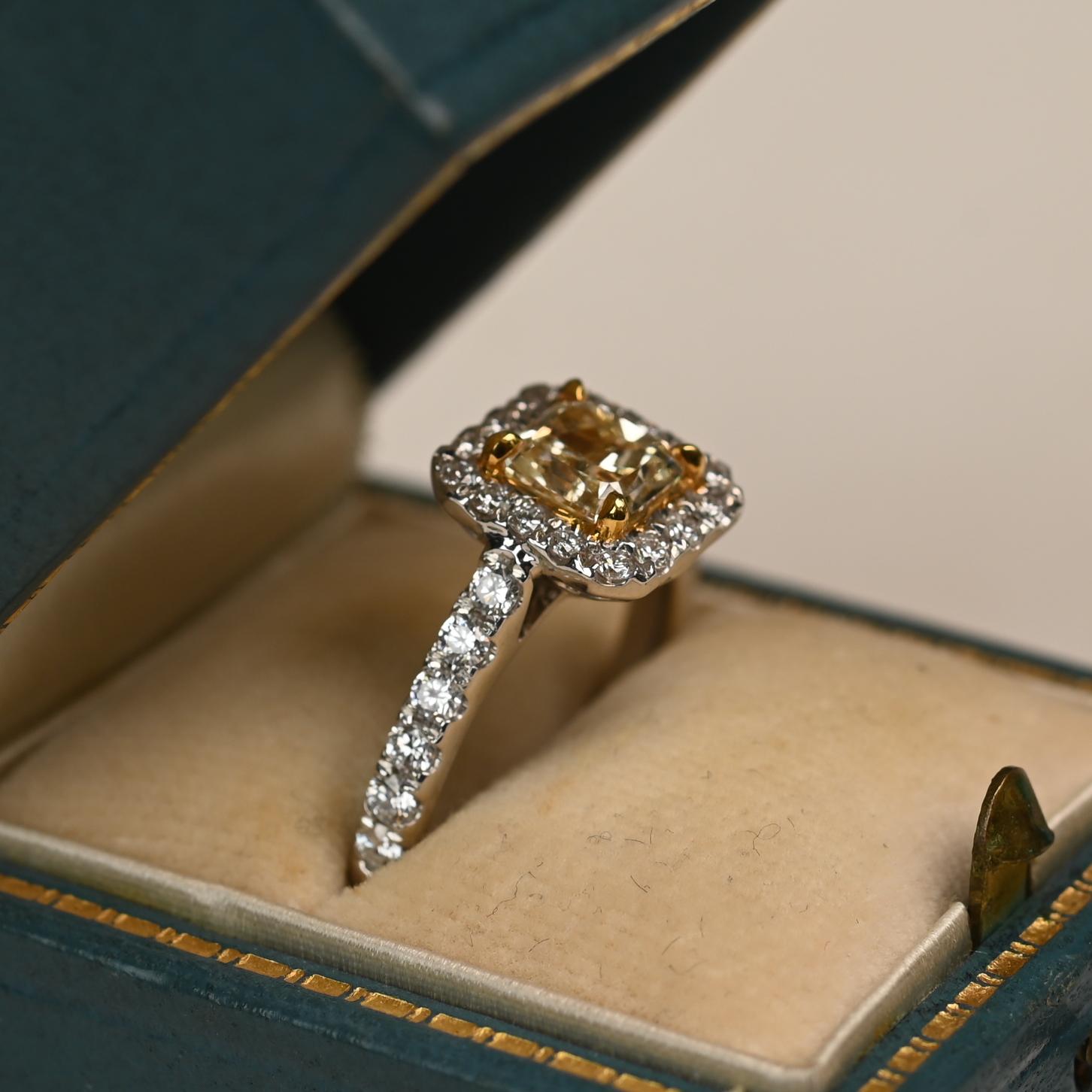 A stunning ring showcasing an approximately 1.10 carat radiant cut yellow diamond, graded VS1 clarity, set in a warm yellow gold prong setting. Surrounding the vibrant center stone is a halo of round brilliant white diamonds, adding brilliance and