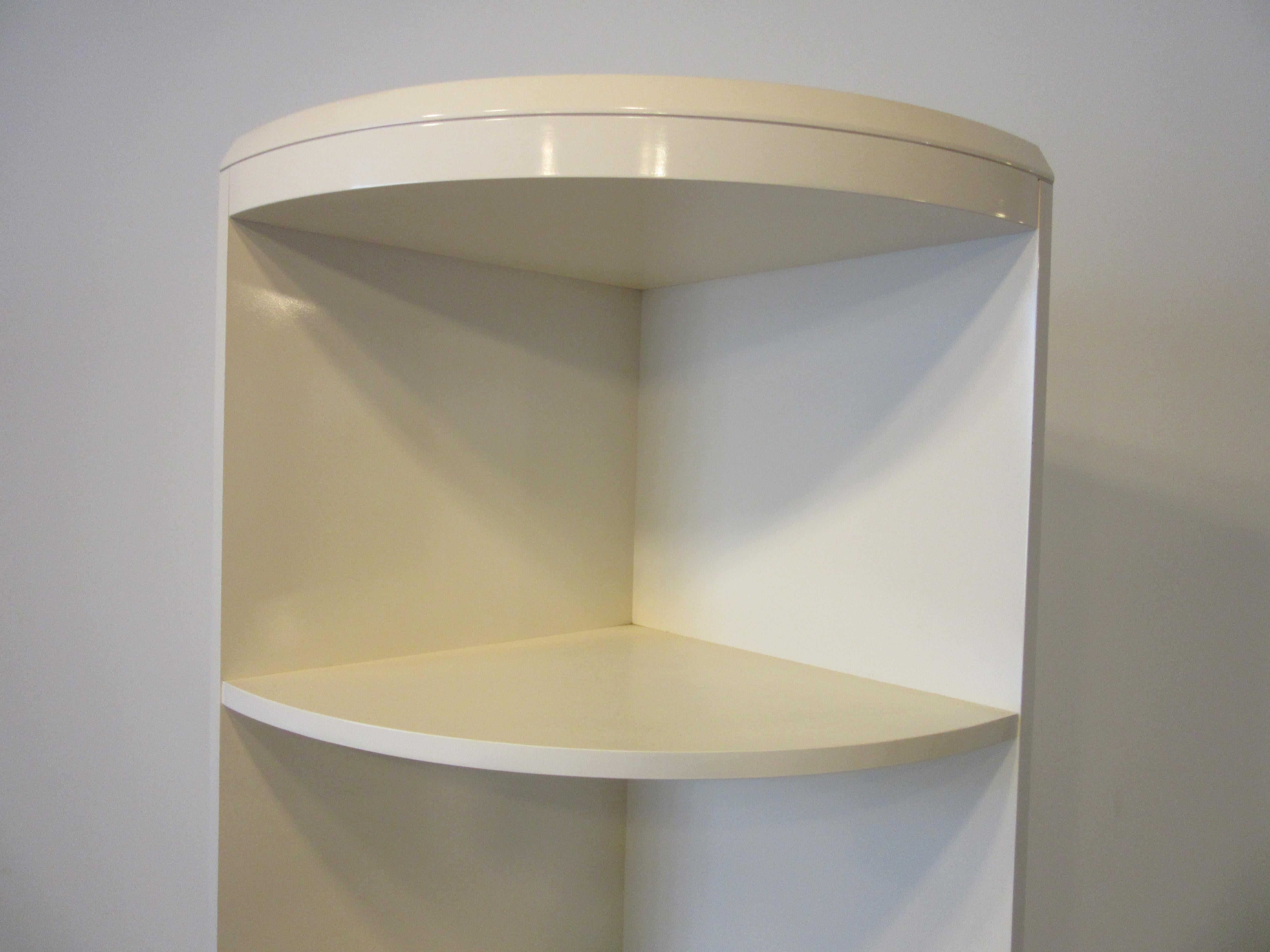 A pair of free standing radius corner bookcase / shelfs with five cubby boxes finished in a creamy white lacquerer having a finished tapered top and a kick to the bottom . Designed in the manner of Karl Springer and perfect to use as extra storage
