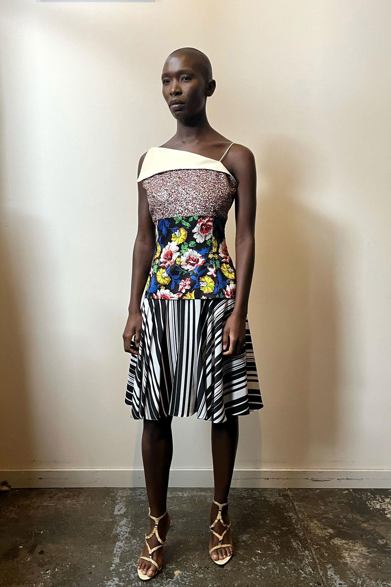 This dress from the 2015 Resort Collection has a dramatic asymmetrical contrast neckline, small straps, and a bodice embellished with multicolor sequins. The fitted waist consists of a colorful floral print, and a black and white striped print makes