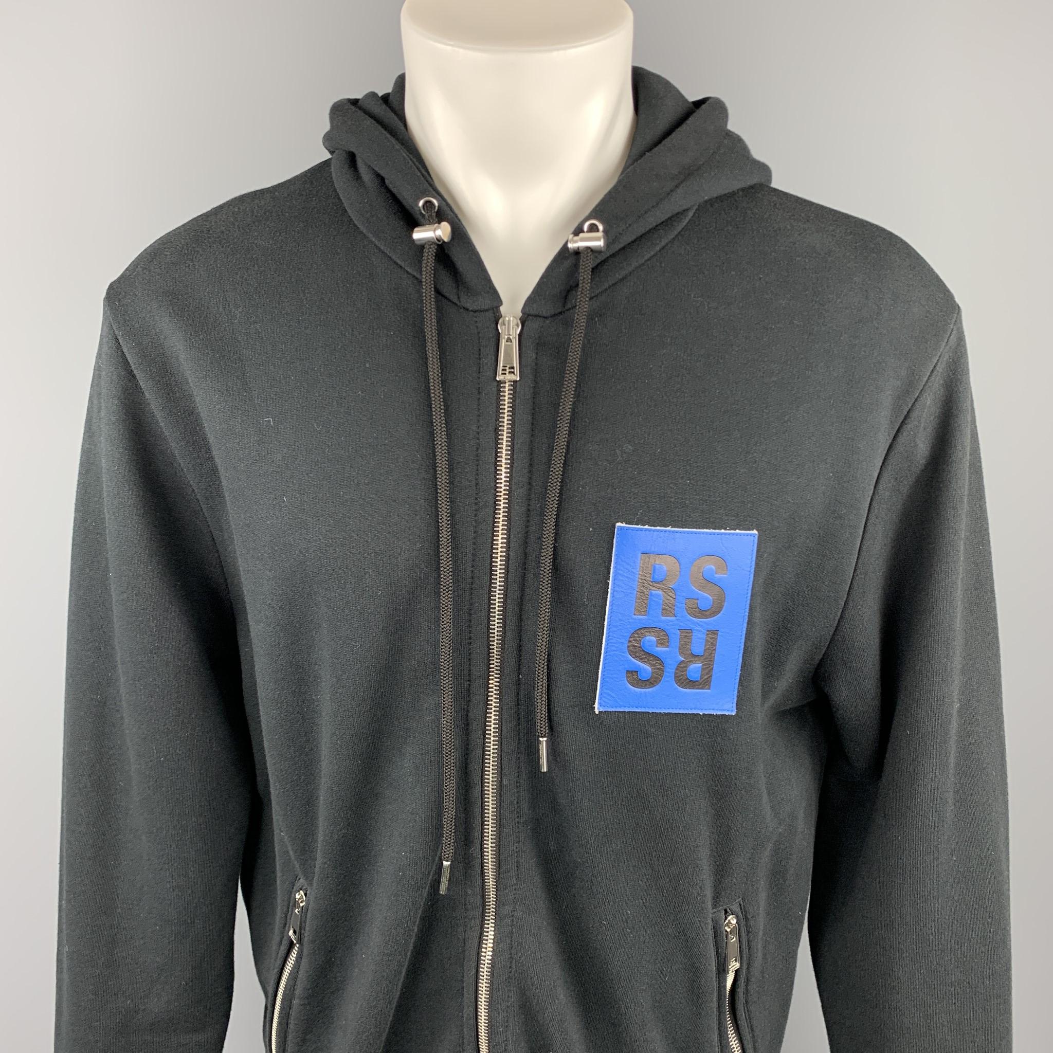 Rare, Iconic RAF SIMONS Fall 2015 - to the archives no longer relevant - newspaper with robot hand print jacket comes in a black cotton with graphic details, blue RS signature detail featuring a hooded style, zipper pockets, and a zip up closure.