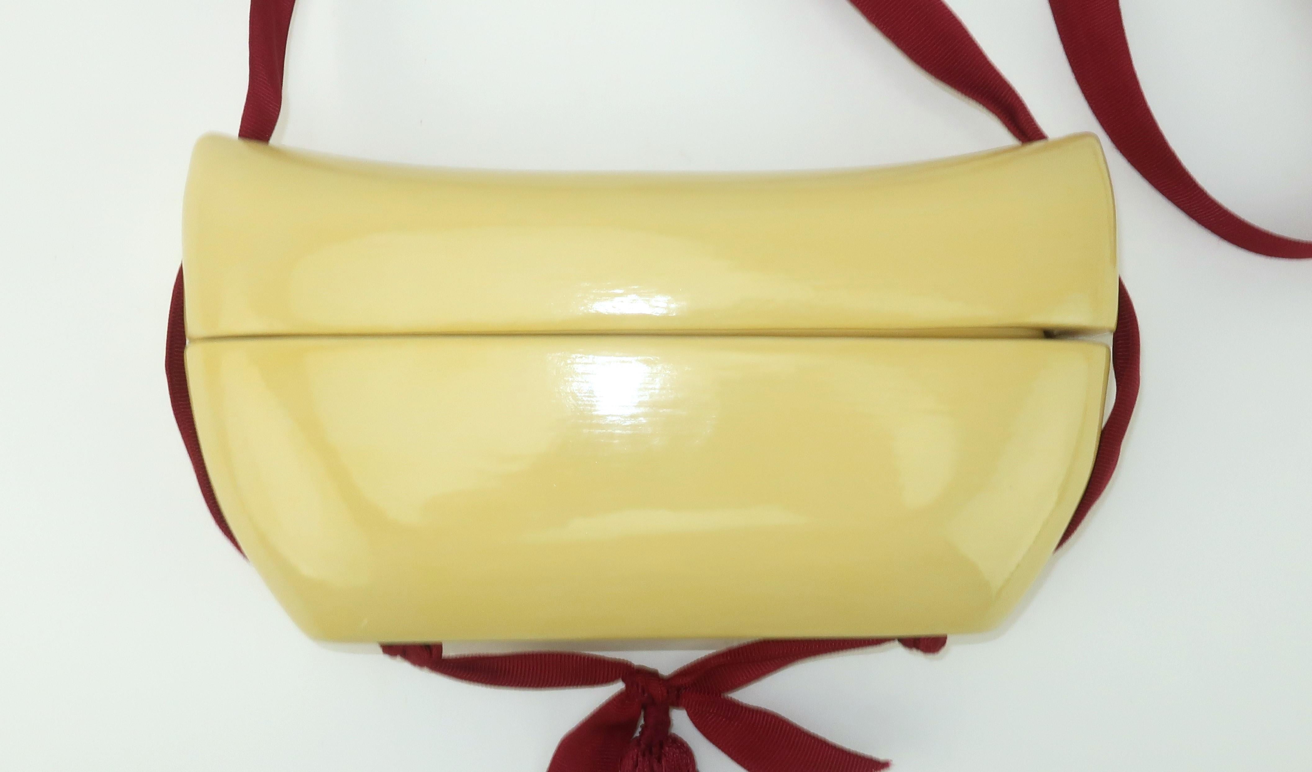 1980's lacquered wood box handbag with an Asian style design in an ivory white shade accented by a burgundy grosgrain ribbon shoulder strap.  The top of the handbag slides up to access the interior and the grosgrain shoulder strap is anchored by a