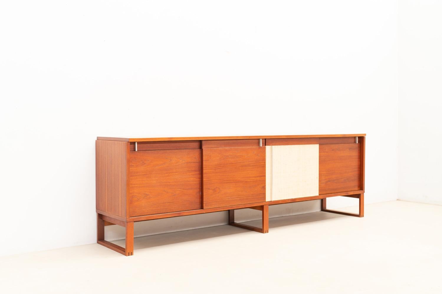 60s sideboard with raffia accent.

This 60s sideboard features four sliding doors that open to reveal large storage spaces. One door is covered in raffia, creating a contrast with the other wooden doors.

The piece showcases a lovely overall