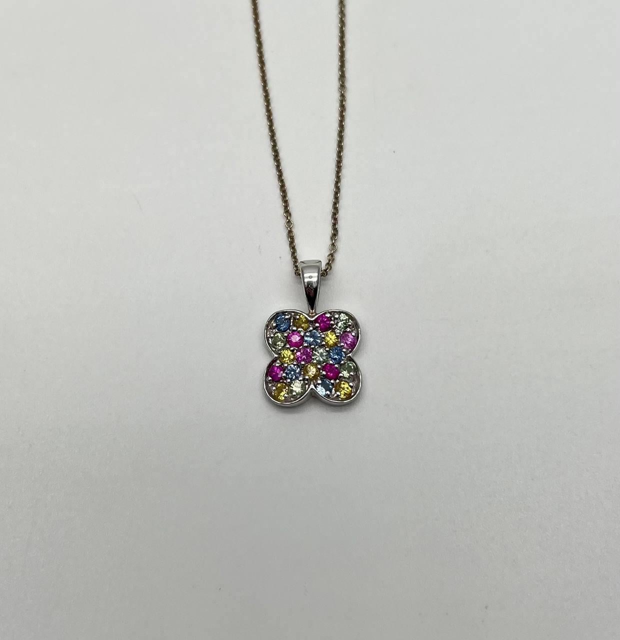 Collier pendentif présentant un motif en forme de trèfle orné de pierres précieuses multicolores. Chaque pétale est serti de pierres rondes dans les tons bleu, rose et jaune. Suspendu à une chaîne délicate. Or blanc 14K. Pierres précieuses de