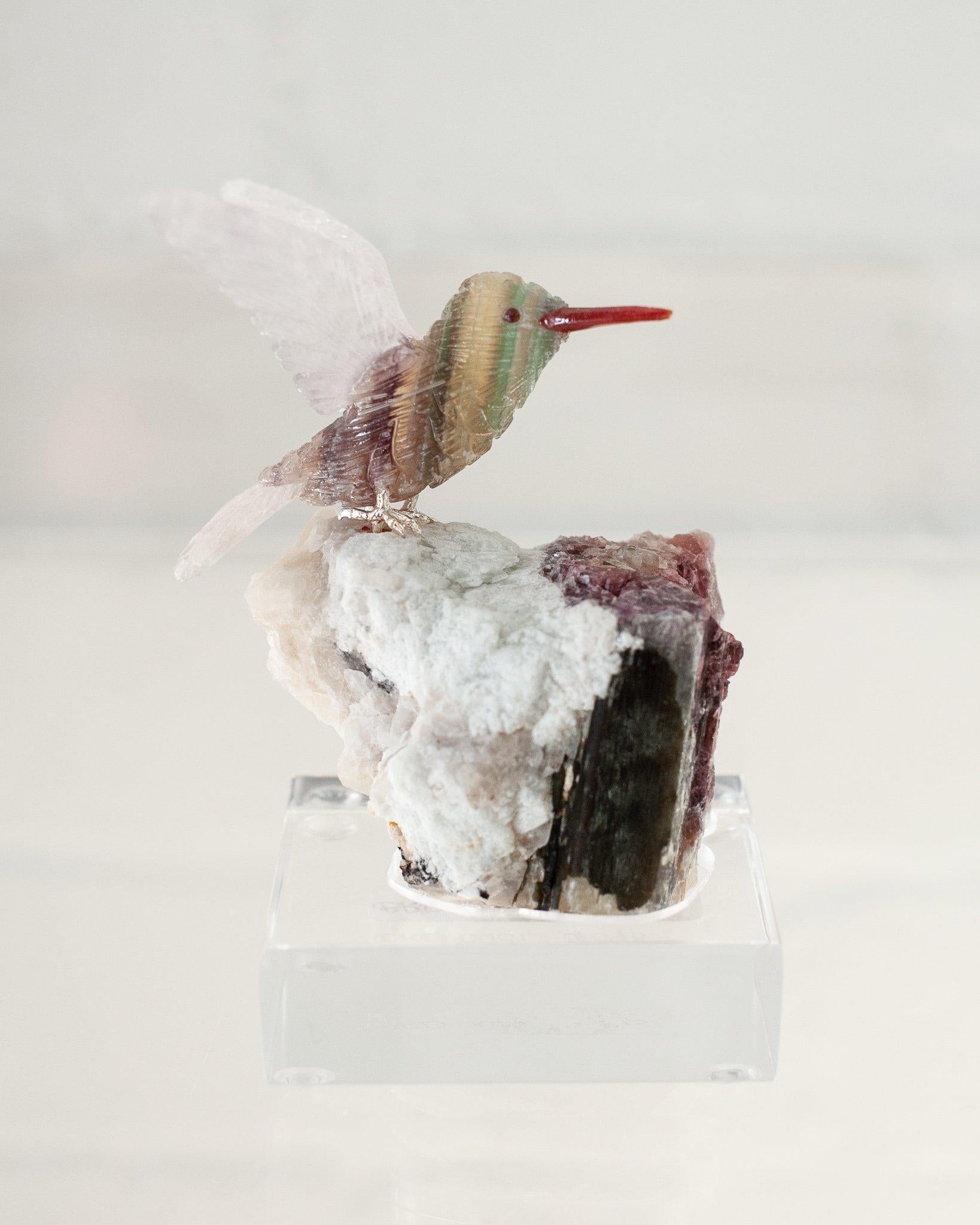 A beautiful hand carved semi precious rainbow fluorite hummingbird mounted on a quartz and tourmaline mineral specimen base. This exotic bird is a decorative combination of ornithology and geology.
