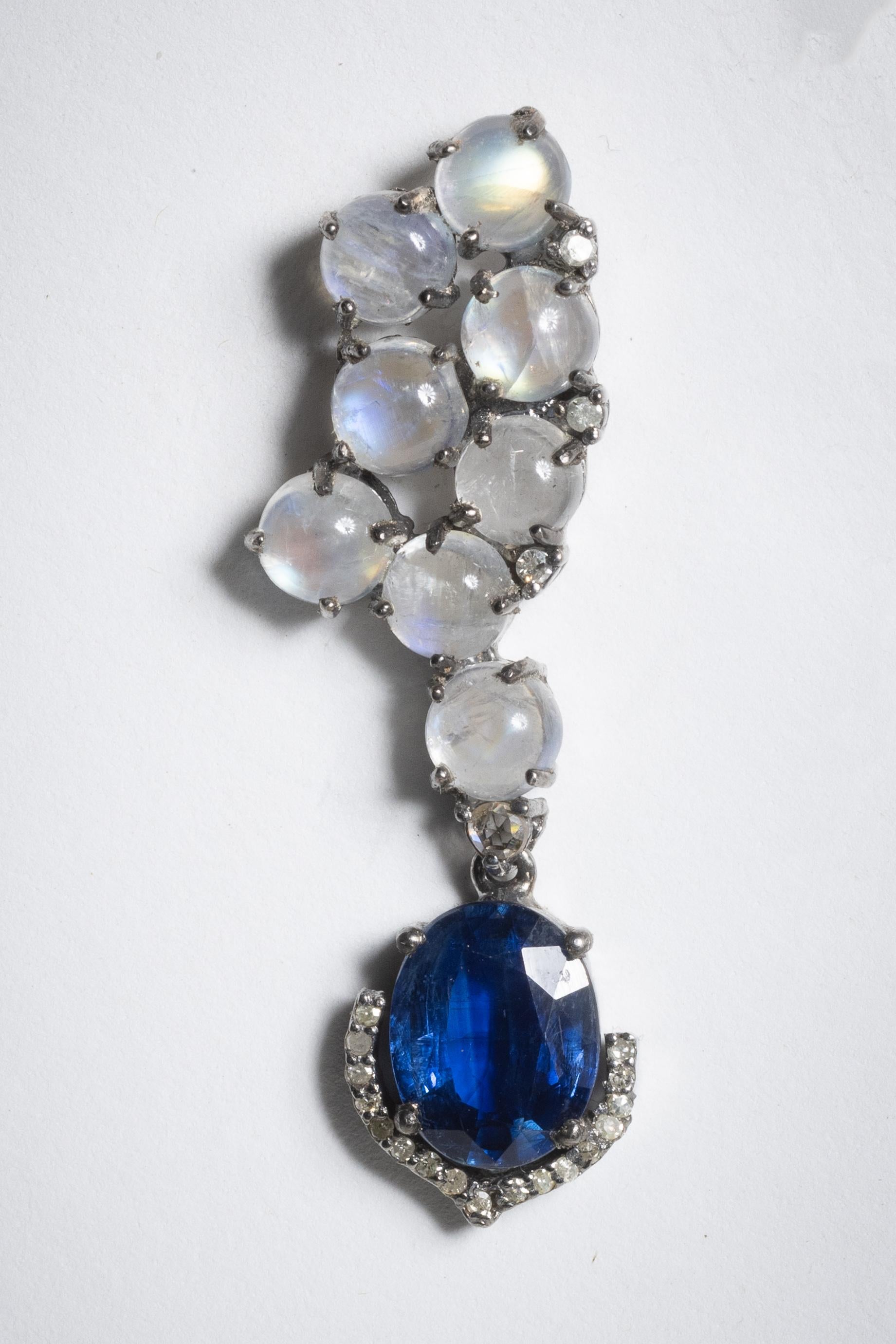 Una bella coppia di pietre lunari cabochon a grappolo con una grande pietra ovale sfaccettata che penzola dalla parte inferiore.  Una fila di diamanti rotondi e sfaccettati a ferro di cavallo circonda la parte inferiore della goccia.  In argento