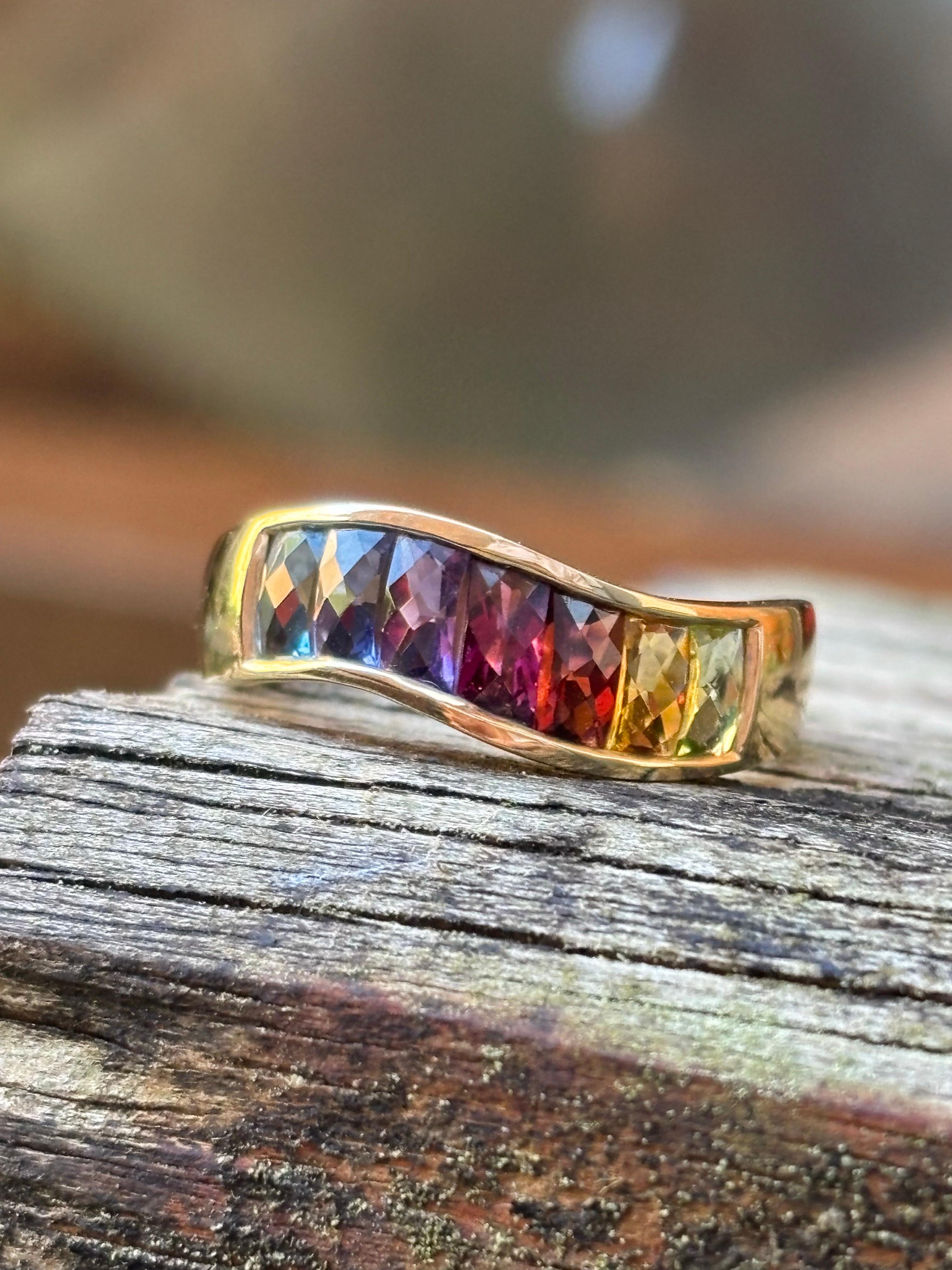 Questo vibrante anello a fascia vintage è splendidamente realizzato in oro giallo 14K e incastonato con un'abbagliante serie di gemme sfaccettate disposte in uno spettro arcobaleno. Le pietre incastonate includono un ricco granato, uno scintillante