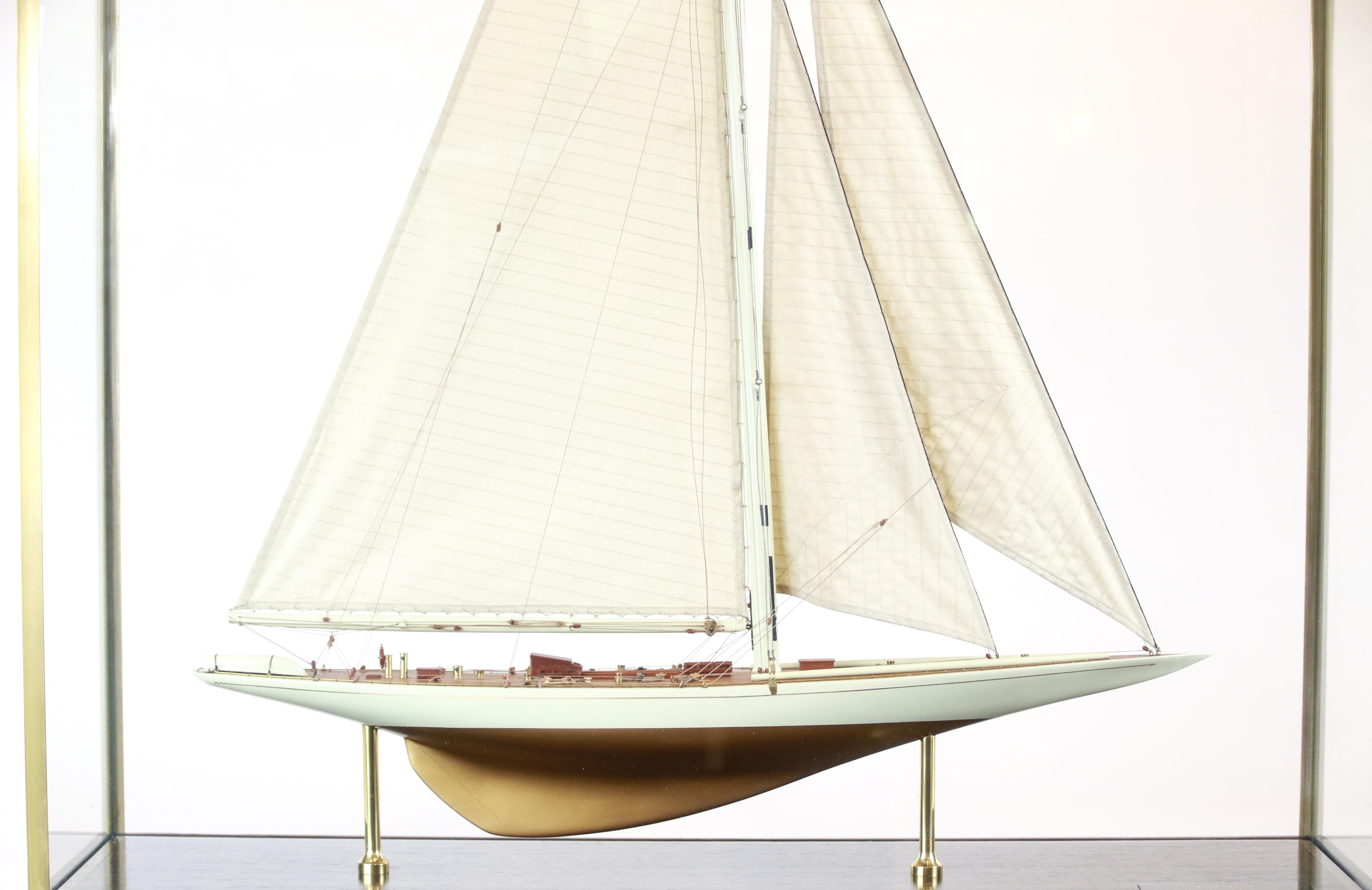New York Yacht Club J-class sloop Rainbow model of 1934. The gold and ivory hull model is detailed with lifeboat, capstan, helm, binnacle, skylights, hatches, boom and a full suit of stitched linen sails. Rainbow is displayed in a glass and brass
