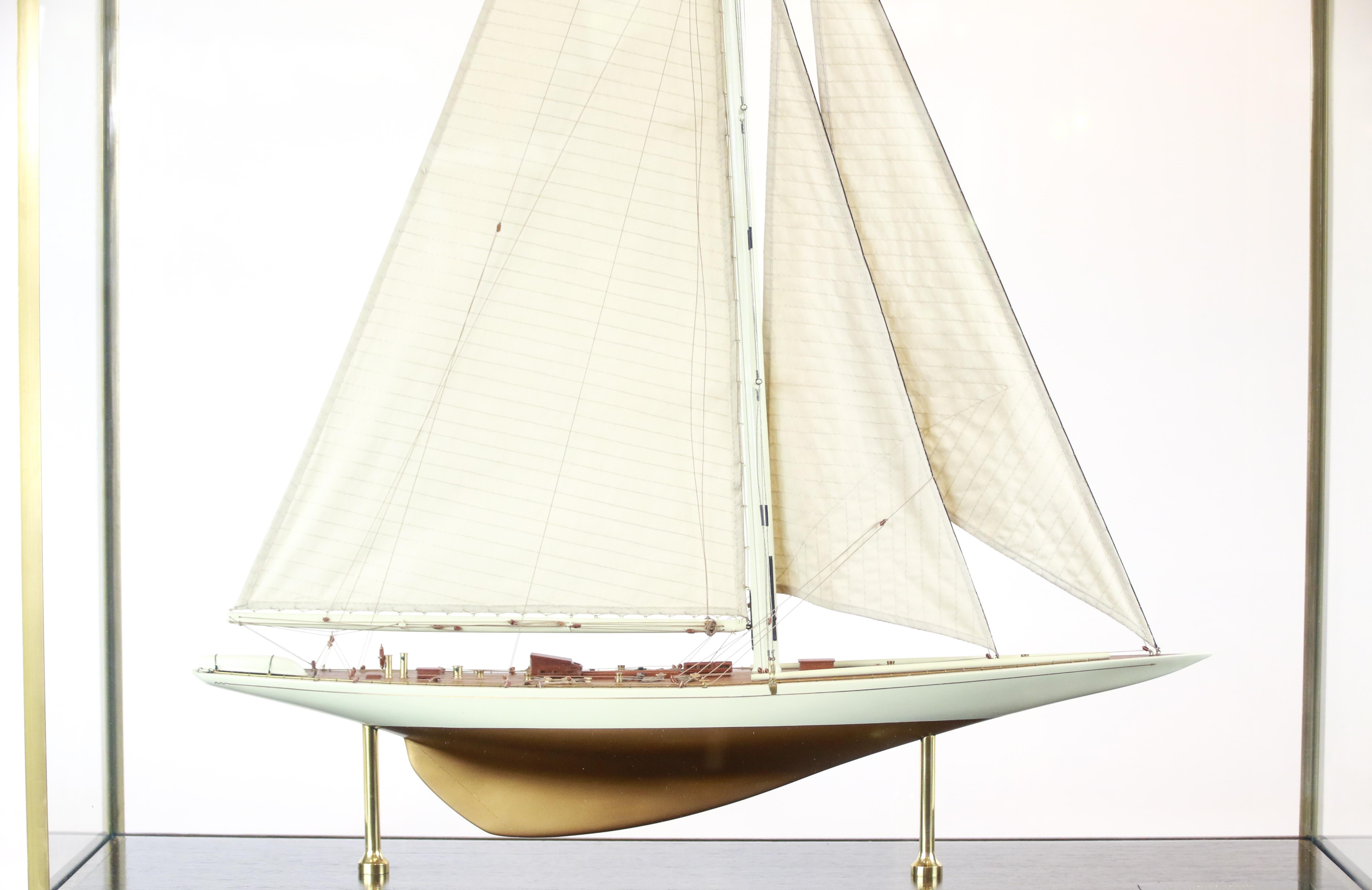 New York Yacht Club J-class sloop Rainbow model of 1934. The gold and ivory hull model is detailed with lifeboat, capstan, helm, binnacle, skylights, hatches, Boom and a full suit of stitched linen sails. Rainbow is displayed in a glass and brass