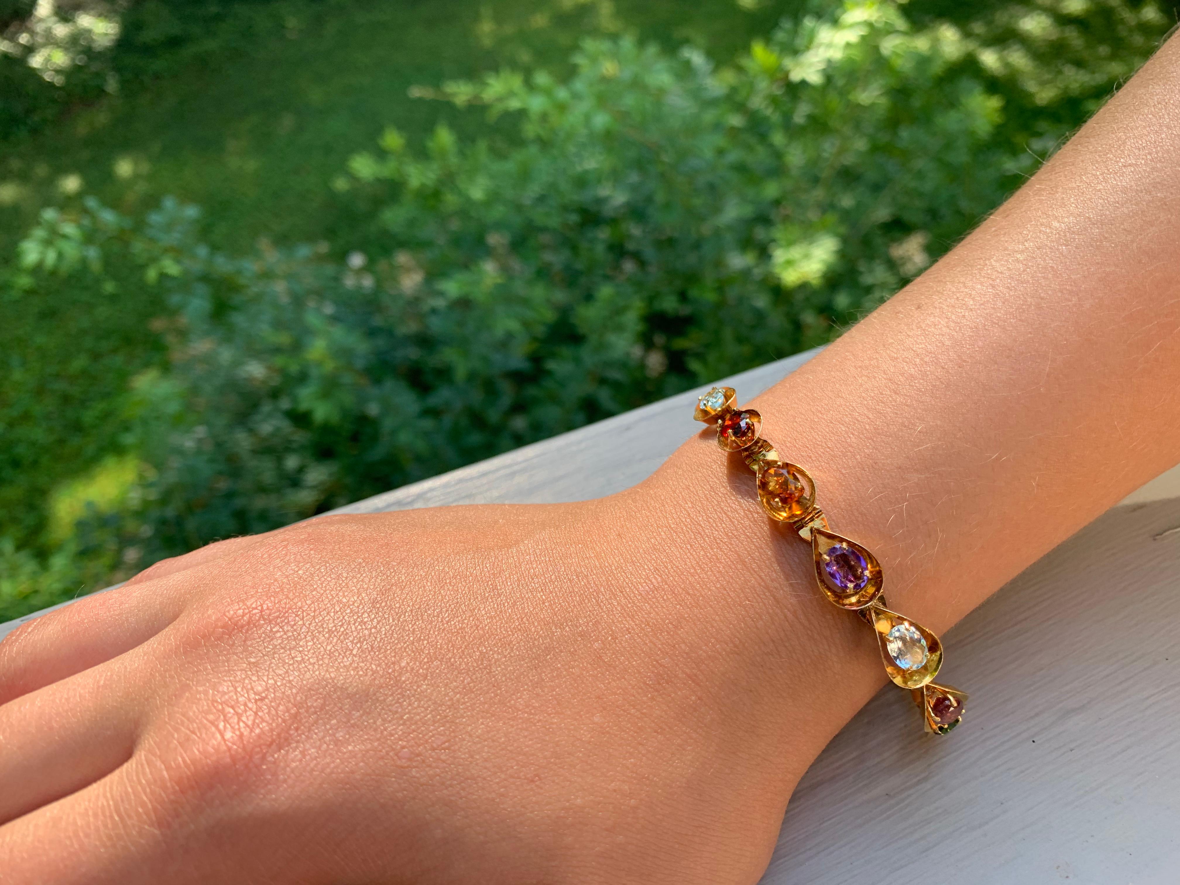 Beautiful European 18K gold multi-colored gemstone bracelet composed of thirteen drop shaped hinged 18K yellow gold links each set with a faceted oval gemstone: garnet, citrine, amethyst, tourmaline, topaz, aquamarine
- A Rainbow of Gemstones. 
Each