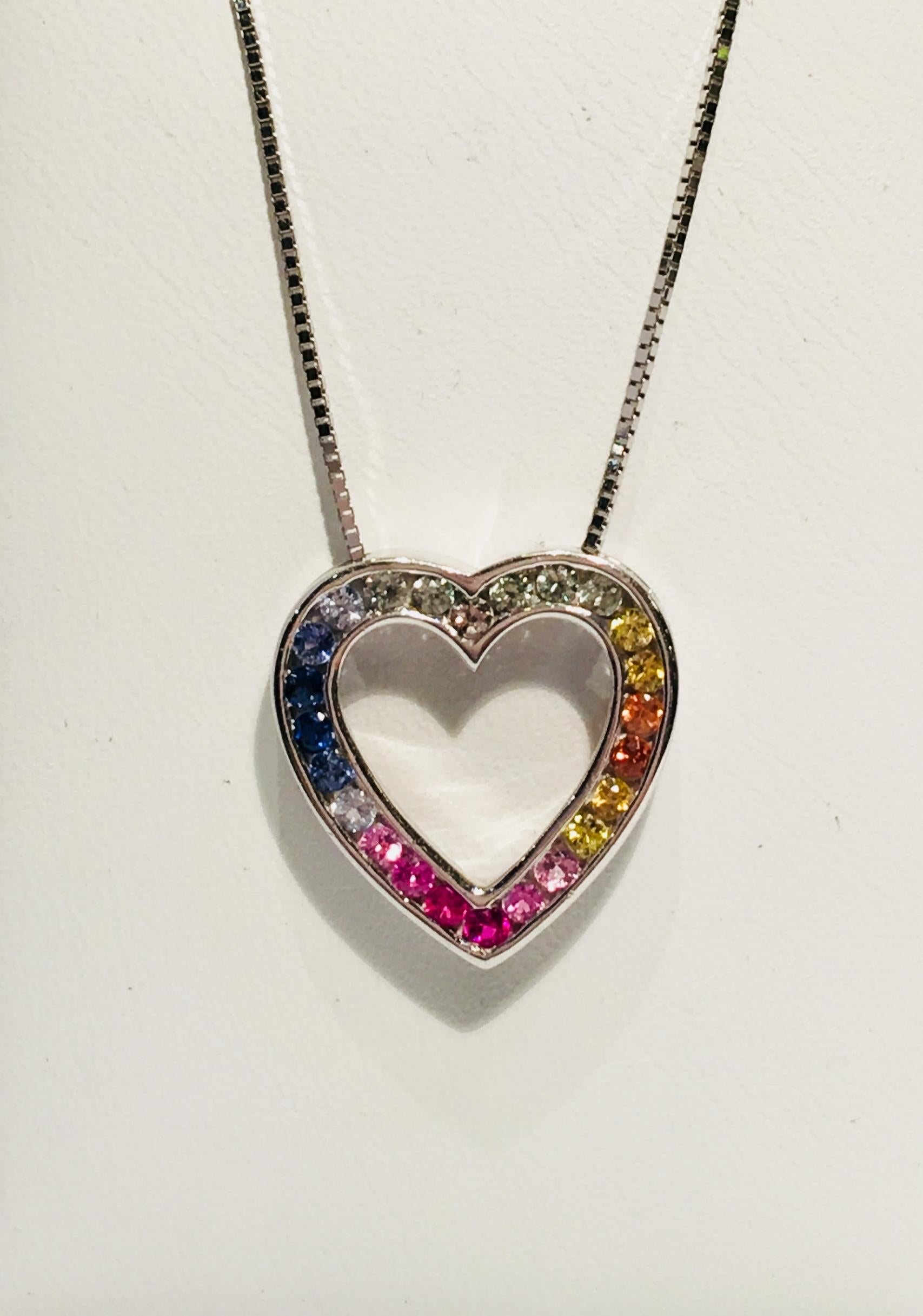 Sweet heart shaped 14 karat white gold pendant features 24 channel set round sapphires in colors of white, yellow, orange, light pink, dark pink, light blue and dark blue, creating a rainbow effect.

Sapphires measure 1.85 mm in diameter and weigh