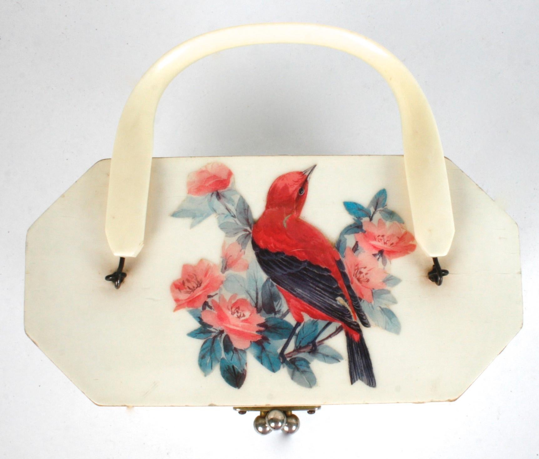 A raised decoupage box handbag by Annie Laurie of Palm Beach. On each side are raised decoupage birds and flowers. The top opens by a gold tone three ball closure and a bakelite handle. The interior is quilted in a grey blue cotton fabric and