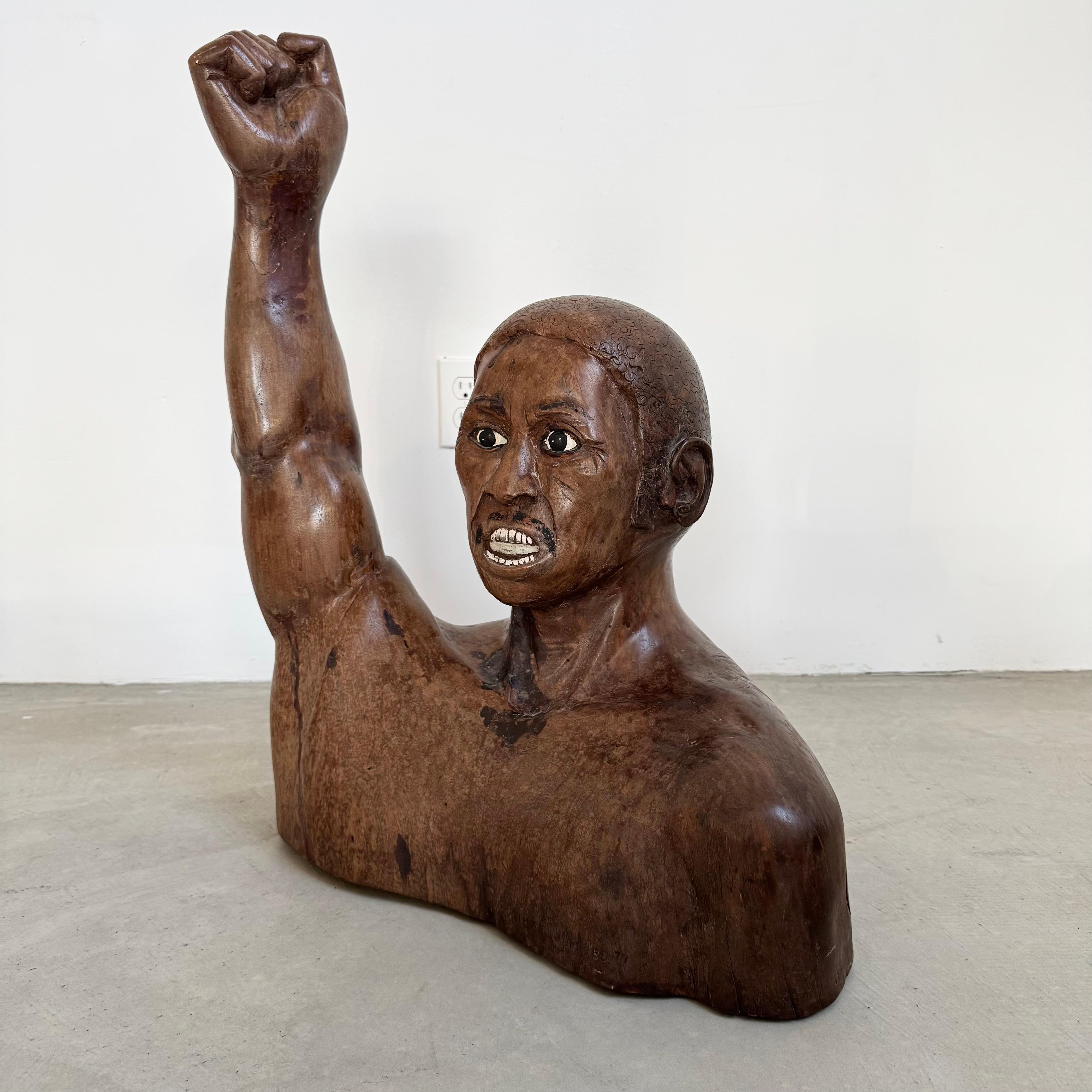 This unique work of folk art is a spirited profession of solidarity and resistance. Hand-carved from a solid piece of wood revealing the bust of a man. His right arm is raised, bearing a clenched fist. His earnest expression is a striking focal