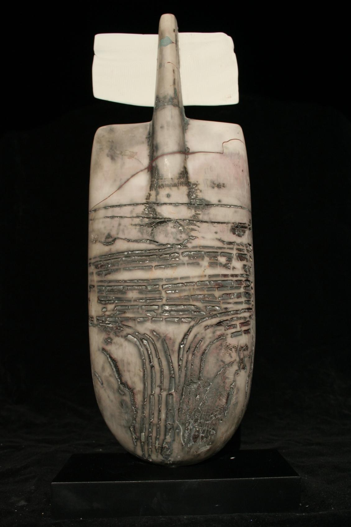 This obelisk shaped object is completely handmade, raku fired ceramic. The surface is textured with ridges and grooves which have a variegated patina due to a natural aging process the artist uses. The artist has adorned top of the sculpture with