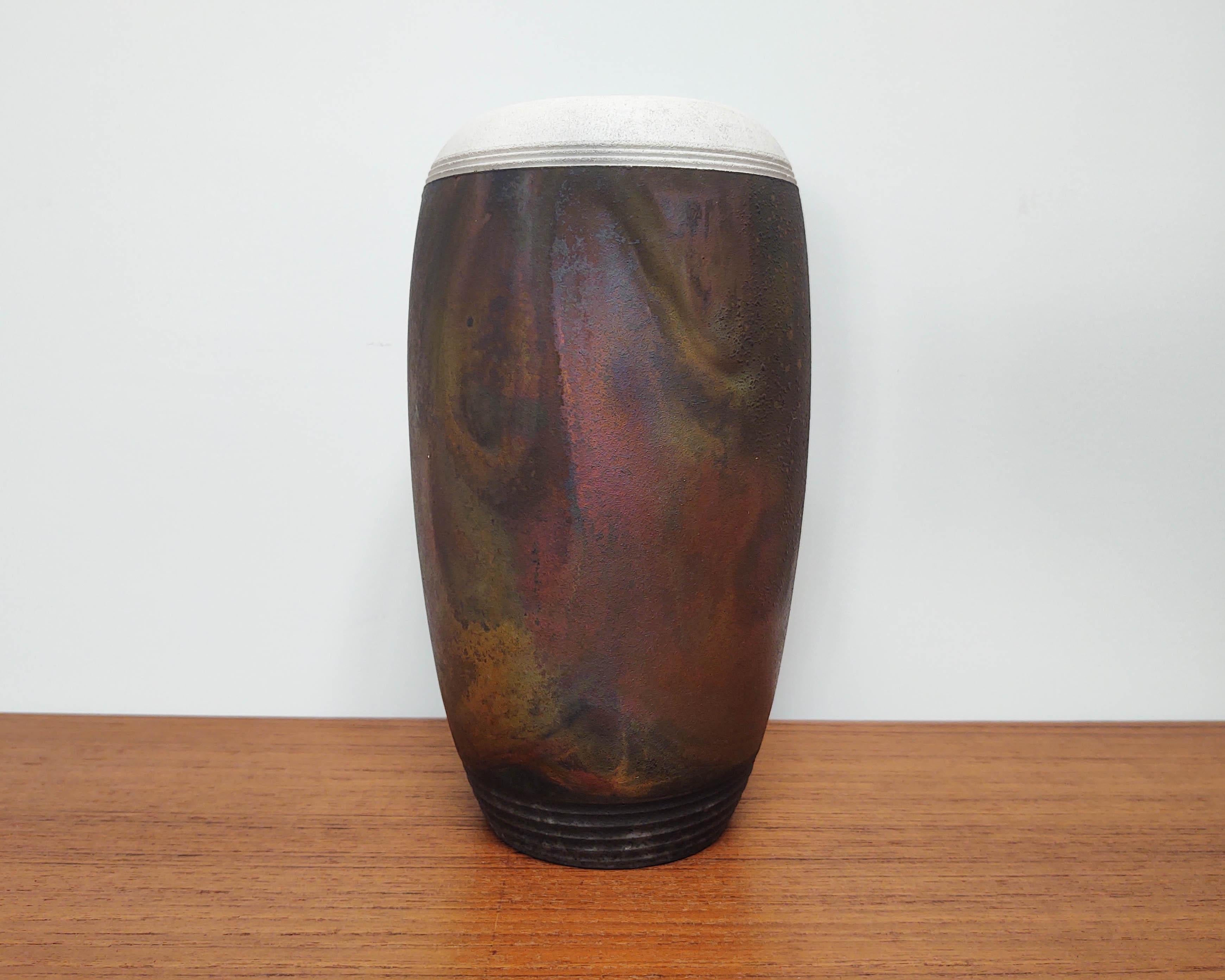 Vase / récipient oblong en céramique noire avec une couche d'oxyde arc-en-ciel tourbillonnante typique de la cuisson raku. Le bord est blanc contrastant et le pied est sculpté en noir. Le vitrage/oxyde n'est pas étanche. La signature n'est pas très
