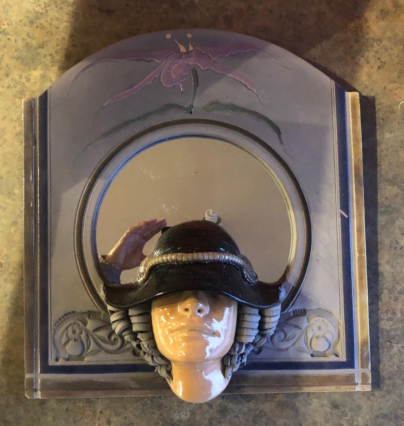 Whimsical raku pottery wall art / mirror with woman's face under a hat signed by Marc Sijan, circa 1980s. The dimensions are 19