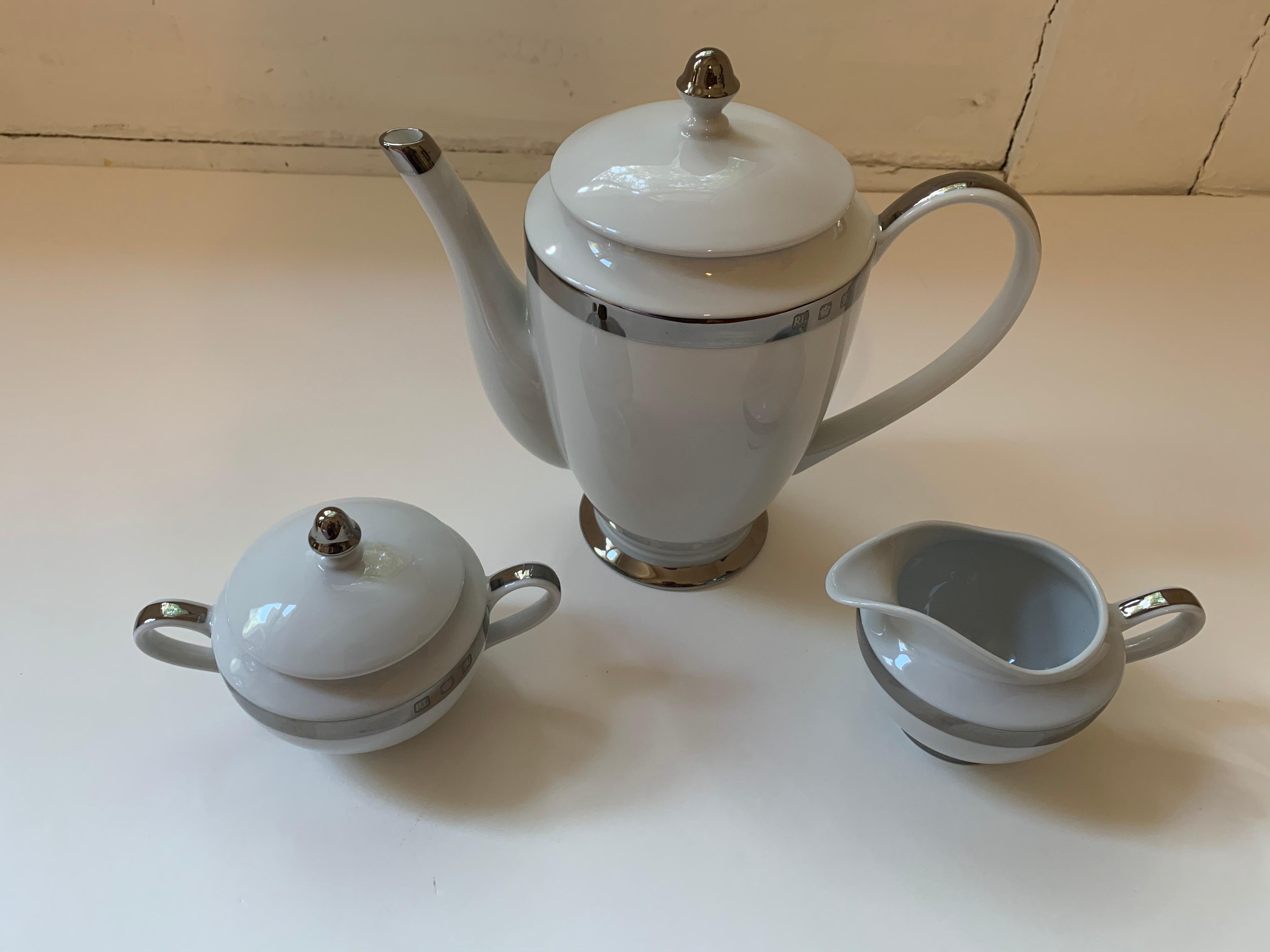 A three (3) piece coffee serving set in the Academy Platinum pattern by Ralph Lauren Home collection. Bone china. Signed. Imported, production period 1995-2002.

Includes a coffee pot with lid, creamer and sugar bowl with lid.

Features a