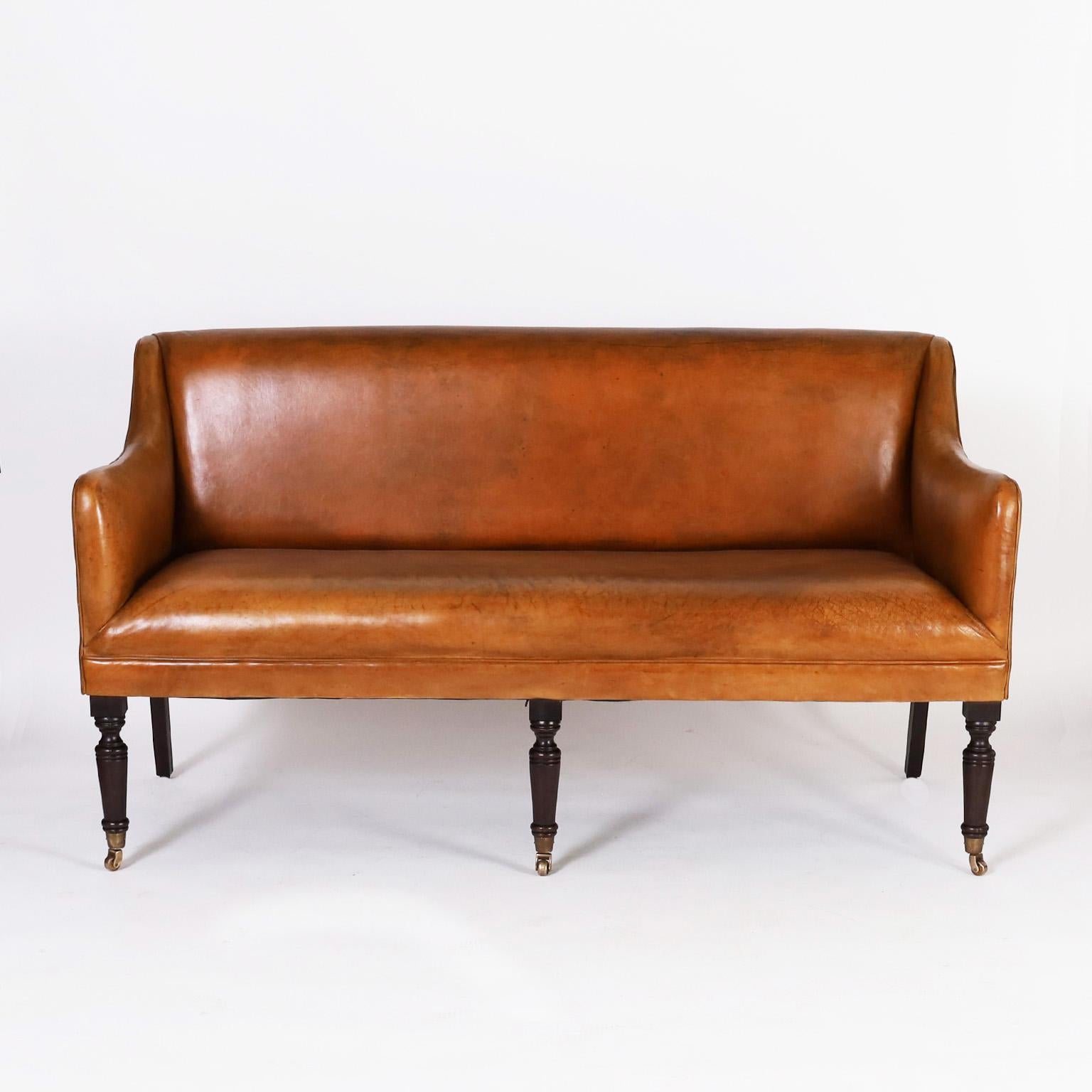 Handsome Georgian style settee upholstered in soft comfortable brown leather in classic form on turned mahogany front legs with brass casters. Signed Ralph Lauren on the bottom.