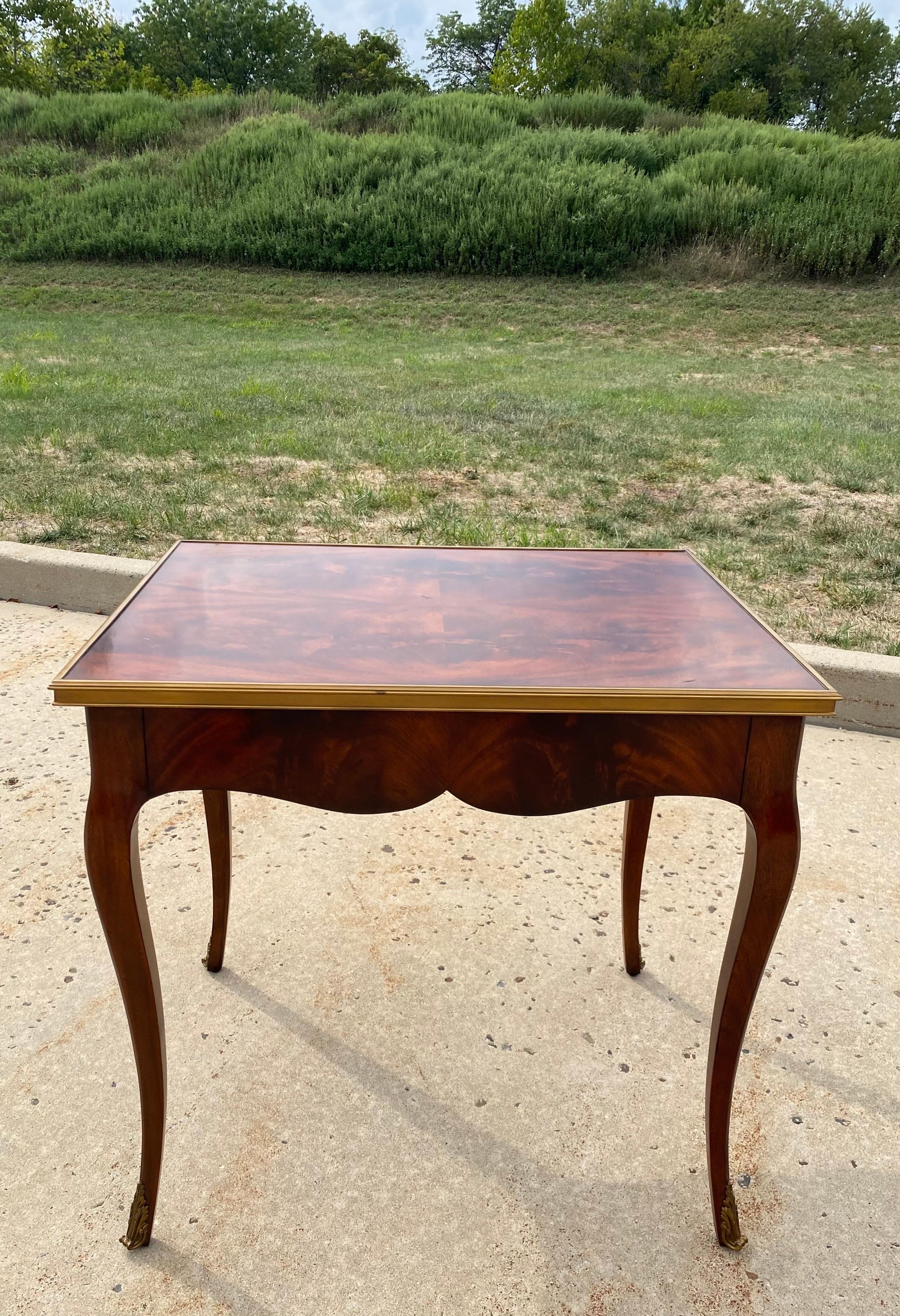 Ralph Lauren home cannes end or bedside table with concealed single drawer. Beautifully patterned Mahogany wood top is trimmed in solid brass. Curved Mahogony wood legs feature decorative brass fittings. This tall rectangular French style table is