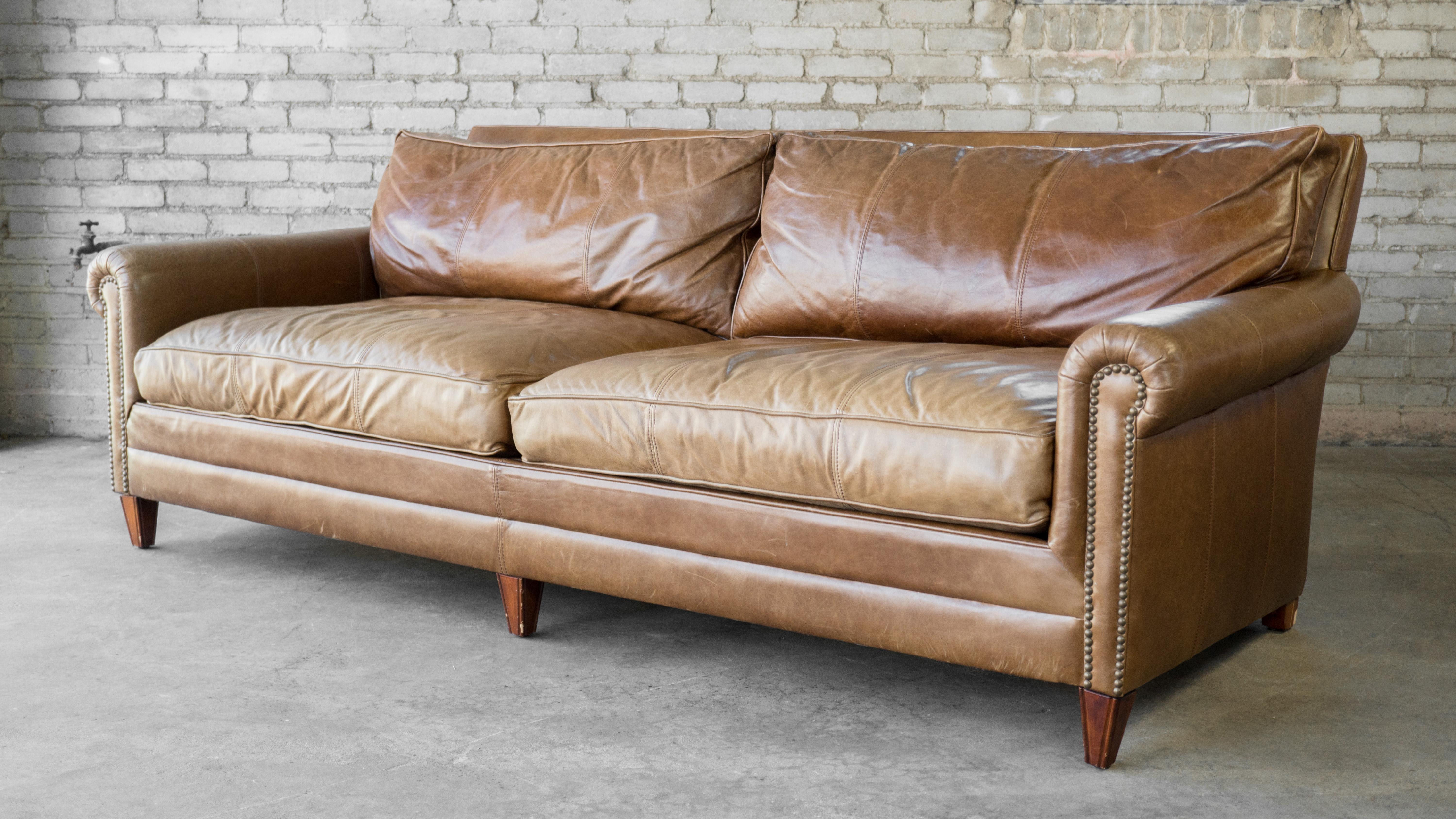 Gorgeous Ralph Lauren MacIntyre leather sofa. Wrapped in beautiful lightly distressed cigar brown leather with thick stitching details. Traditional English roll-arm style with paramount elegance and comfort. Brass nailhead trim. Oversized