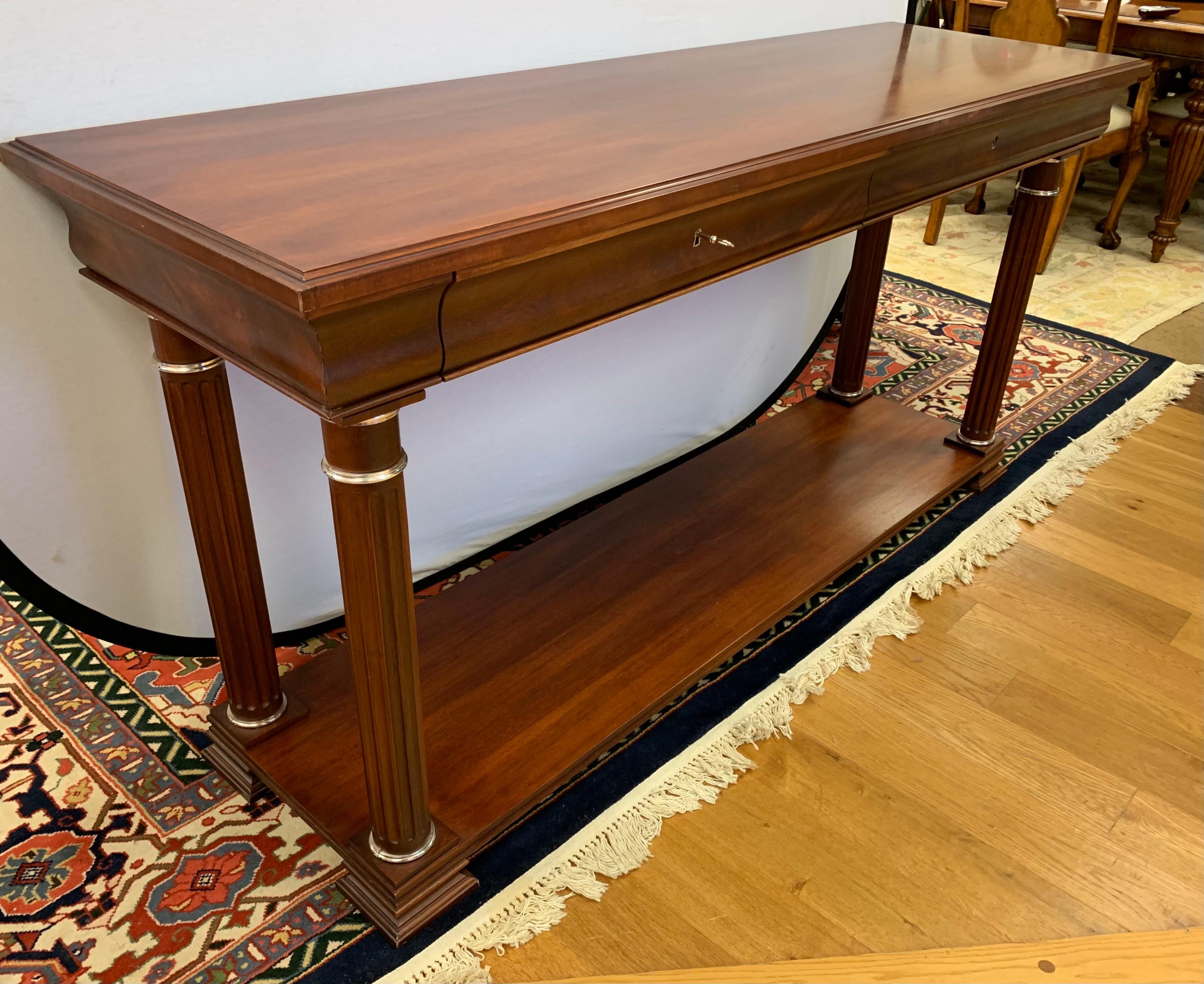Ralph Lauren mahogany console table has two drawers with working lock and key and a bottom shelf. It rests on four fluted legs with brass accents. Marked inside drawer.