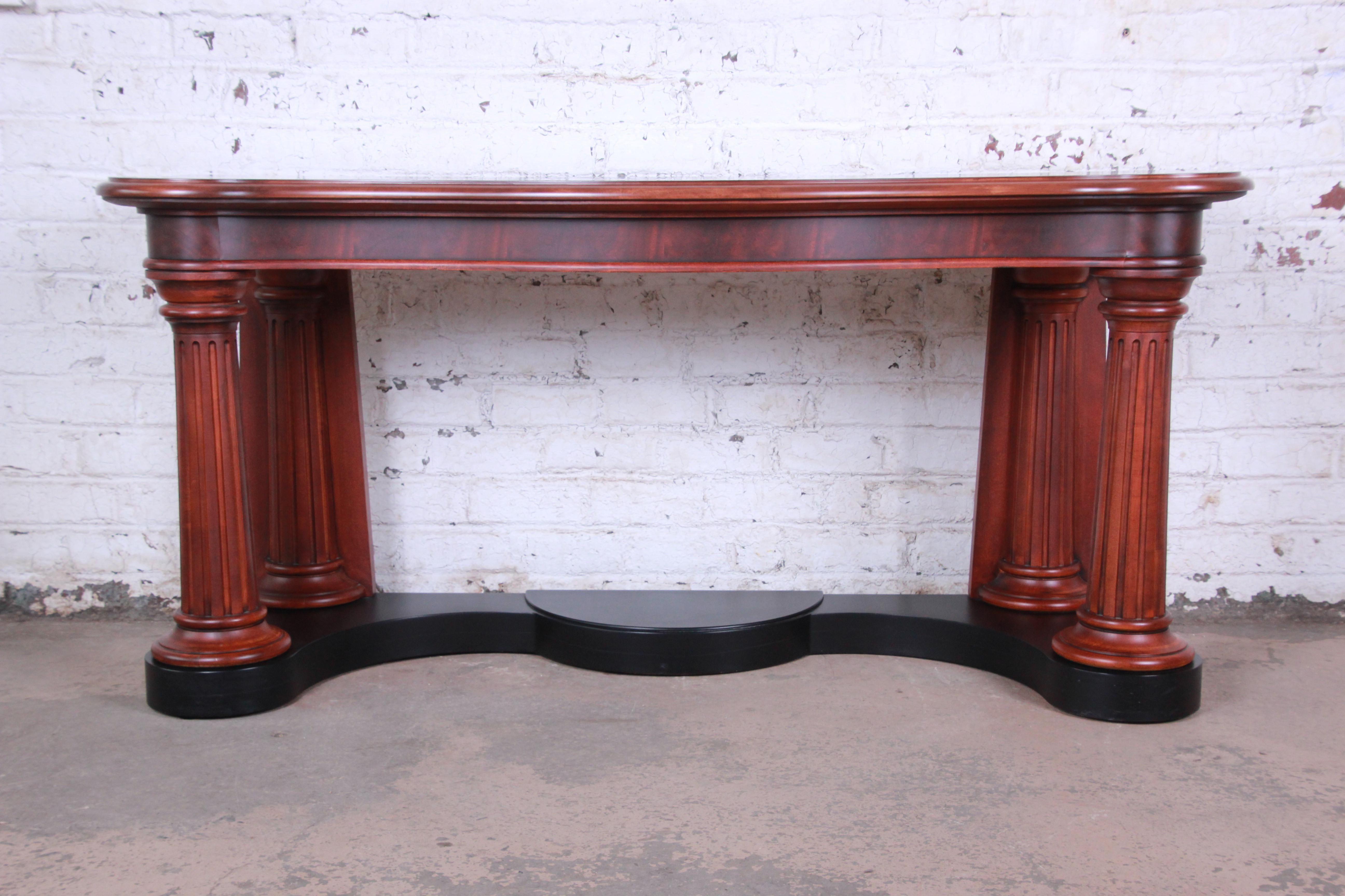 An outstanding neoclassical style console table designed by Ralph Lauren. The table features gorgeous flame mahogany wood grain and a nice Traditional Design. The curved top rests on tall columned legs, with a black lacquered base. The tabletop has