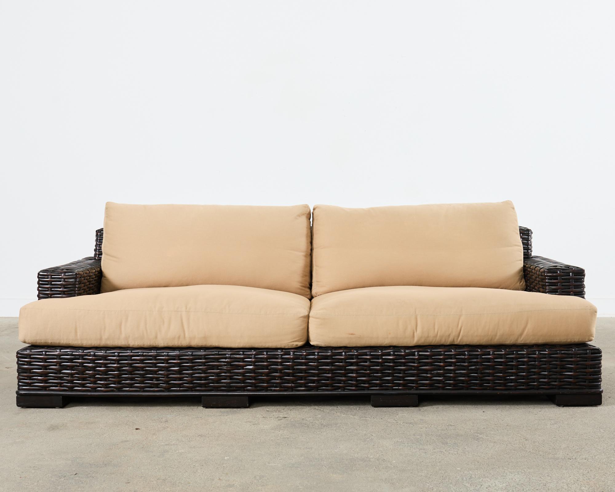 imposing sofa crafted from woven rattan in the organic modern coastal style by Ralph Lauren. The canyon sofa features an oversized hardwood frame completely covered with woven split reed rattan in a dramatic black mahogany finish. The frame is