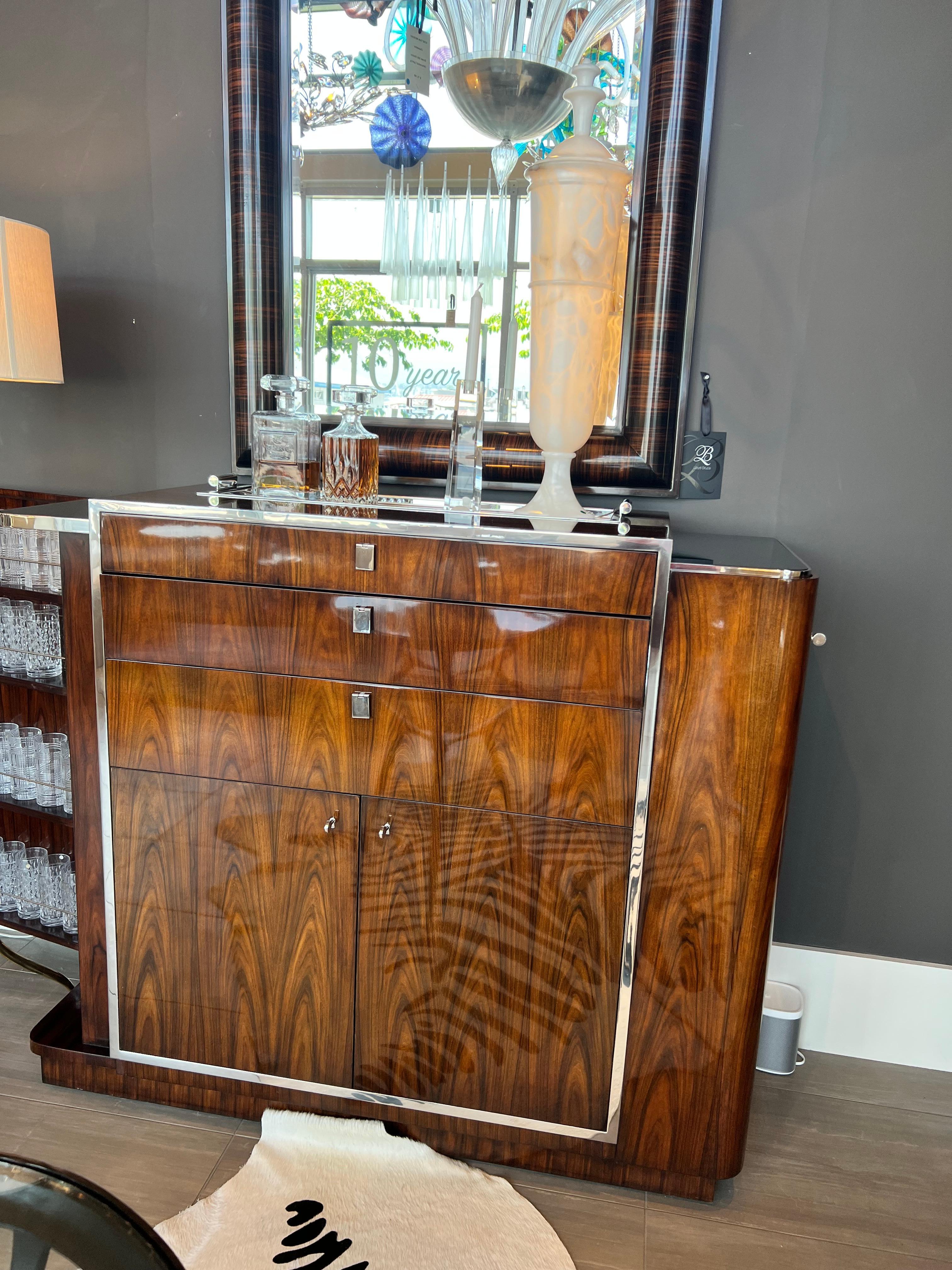 This beautiful dry bar is designed by Ralph Lauren.
It has rosewood veneer and nickel plating. The top tray is removable. Top drawer felt lined. Second drawer pulls out as an additional serving area with smoked glass surface.
Glass and bottle