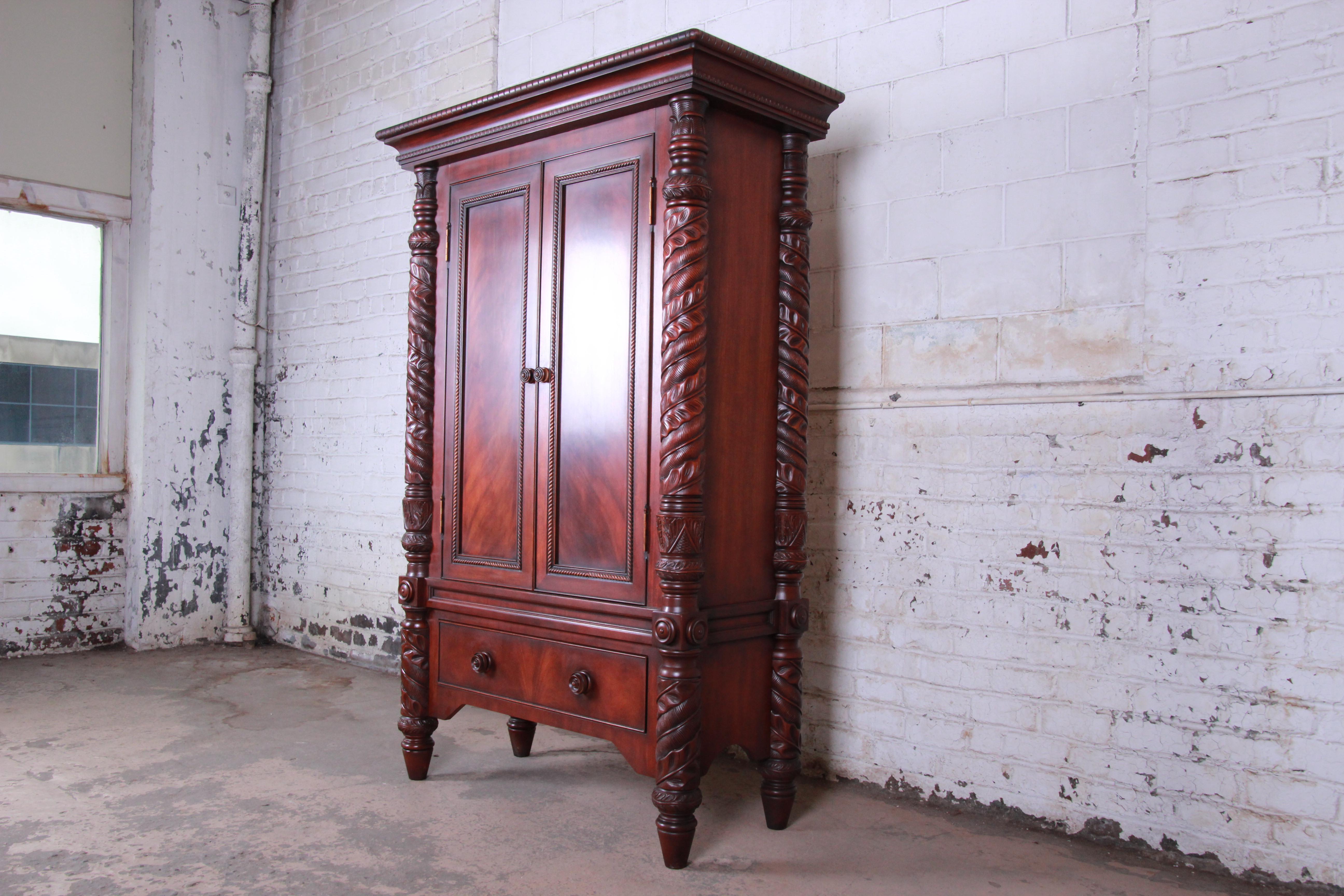 An exceptional mahogany armoire dresser from the Safari collection by Ralph Lauren. The armoire features gorgeous flame mahogany wood grain and ornately carved solid mahogany post legs with a tobacco leaf motif. It offers ample storage, with three