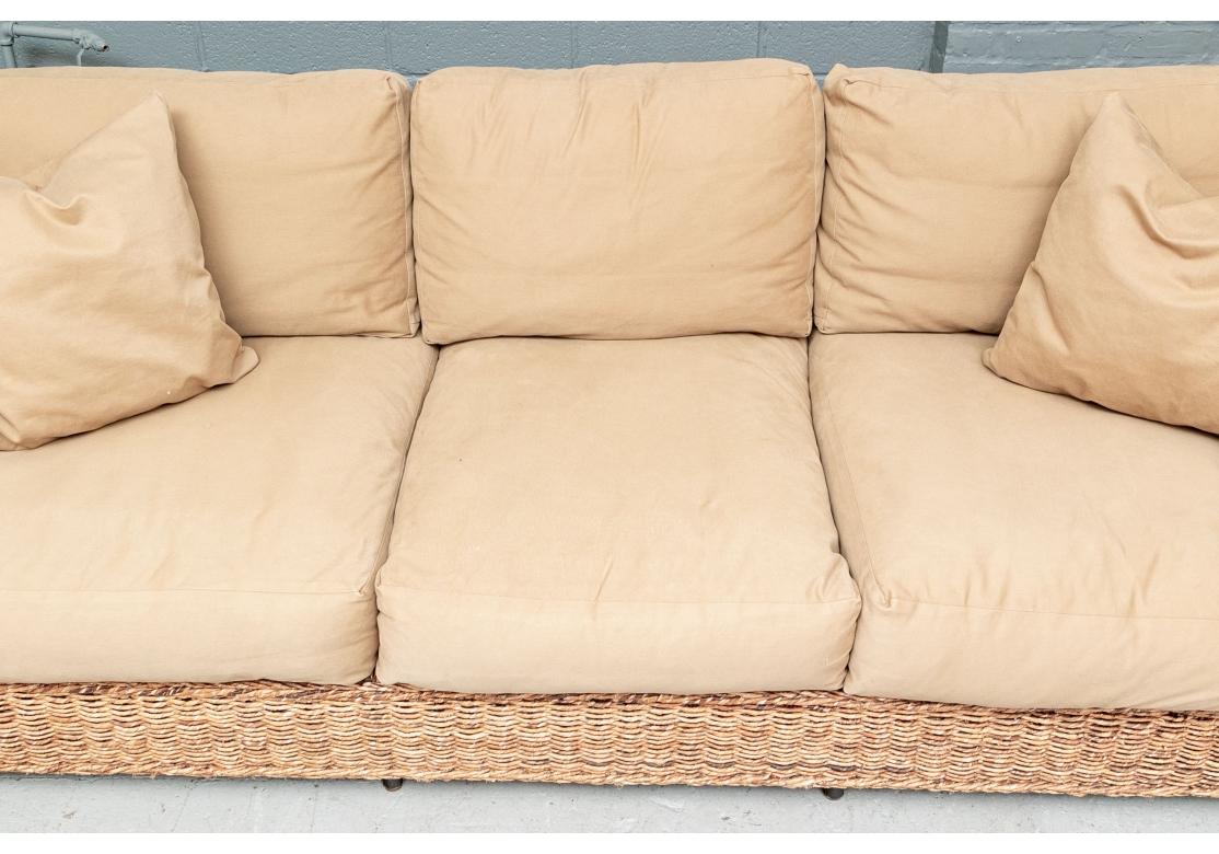 A sumptuous beach house or cabana style sofa from Fashion House Ralph Lauren. A large comfortable woven rope sofa with a square frame, raised on flat dark stained wood legs at the corners. With tan canvas covered cushions and pair of toss pillows.