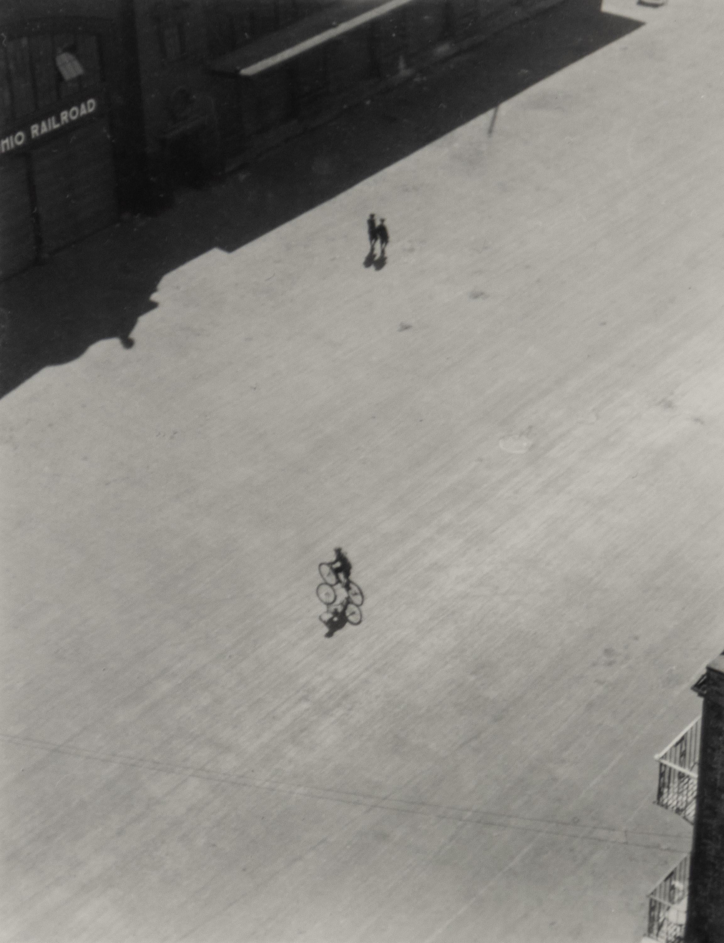 A black and white photograph of an urban plaza with a person on a bicycle. 

Untitled [Bicycle with Shadow], black and white photograph by Ralph Steiner

Untitled [Bicycle with Shadow]
1922

Vintage gelatin silver print

4.75 x 3.5 inches,