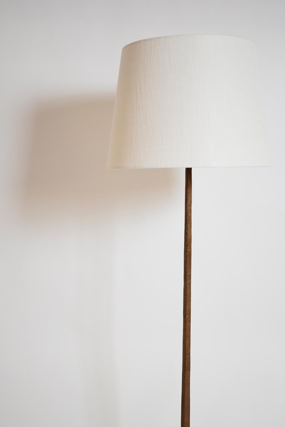 Lampadaire en fer forgé à patine dorée sur une base tripode supportant une tige de section carrée évidée à l'arrière pour le passage du fil. France, années 1960.