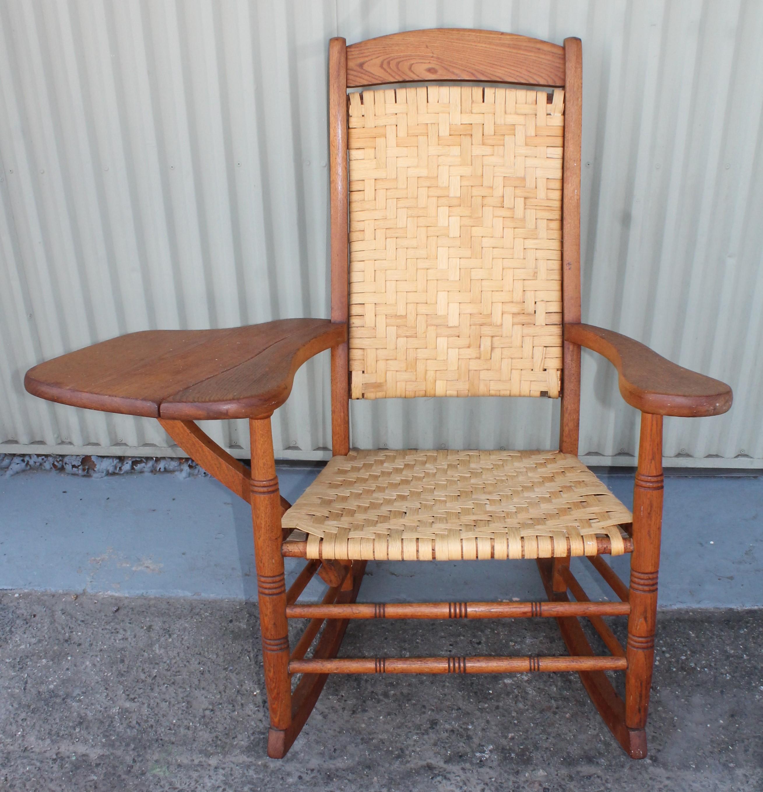 This writing arm rocking chair is from a log cabins front porch and is super comfortable. It is newly re-woven slat seat and backing. This is such great rare form. It is all in old yellow oak. Great inside or out of your country rustic